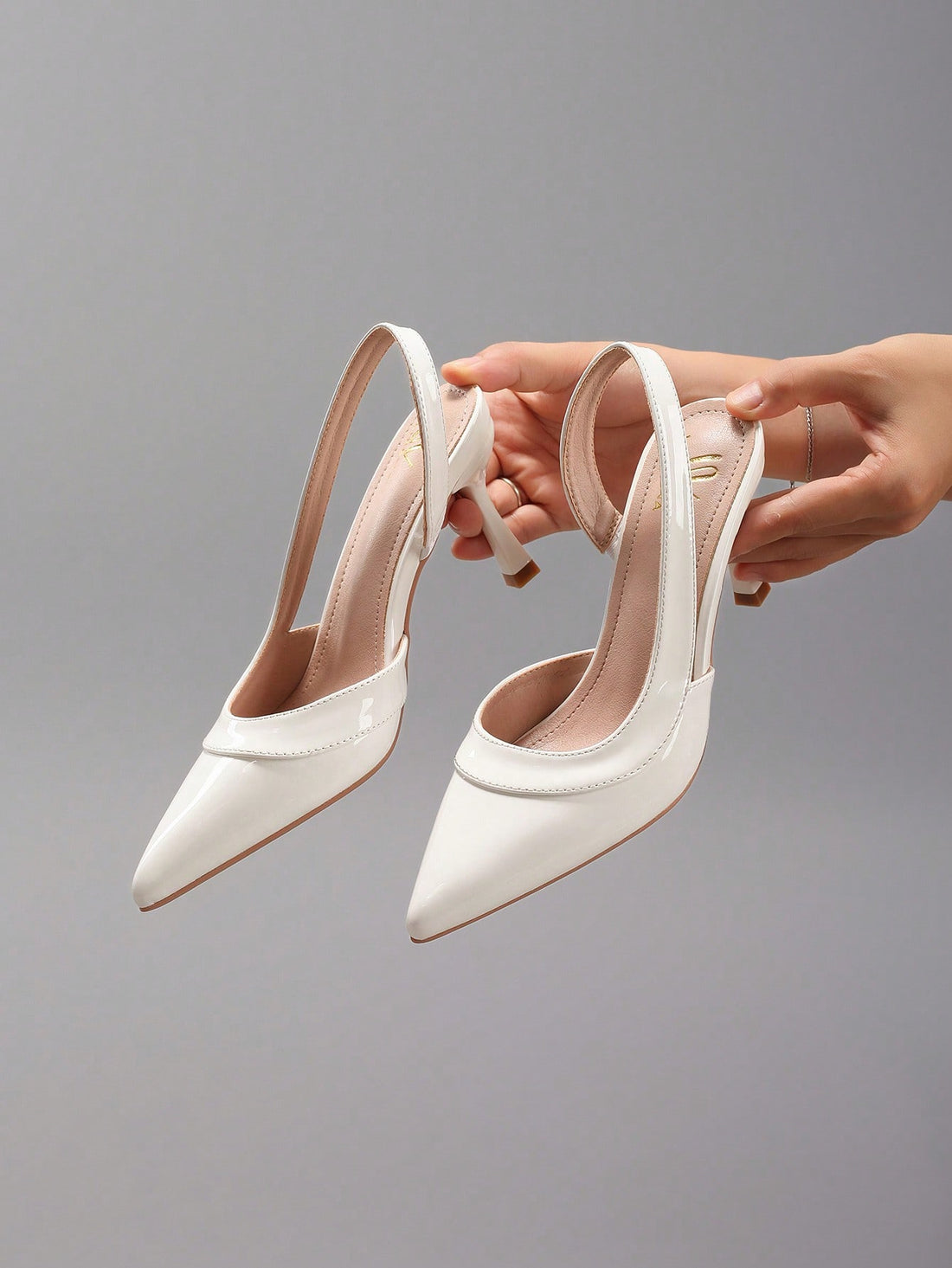 Pair of women's white pointed-toe kitten heel pumps with slingback straps and sleek patent finish