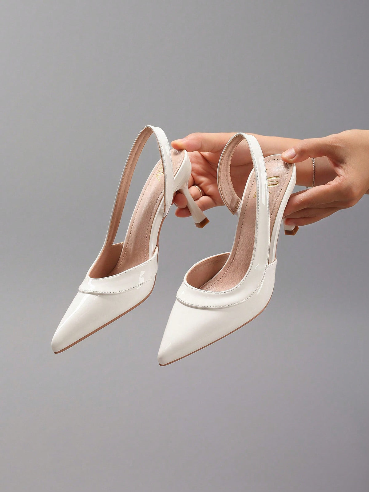 Pair of women's white pointed-toe kitten heel pumps with slingback straps and sleek patent finish