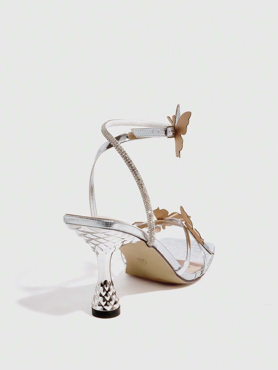 Glossy gold high heels featuring a sculptural heel, open-toe design, ankle strap buckle closure, and sparkling rhinestone butterfly embellishments.