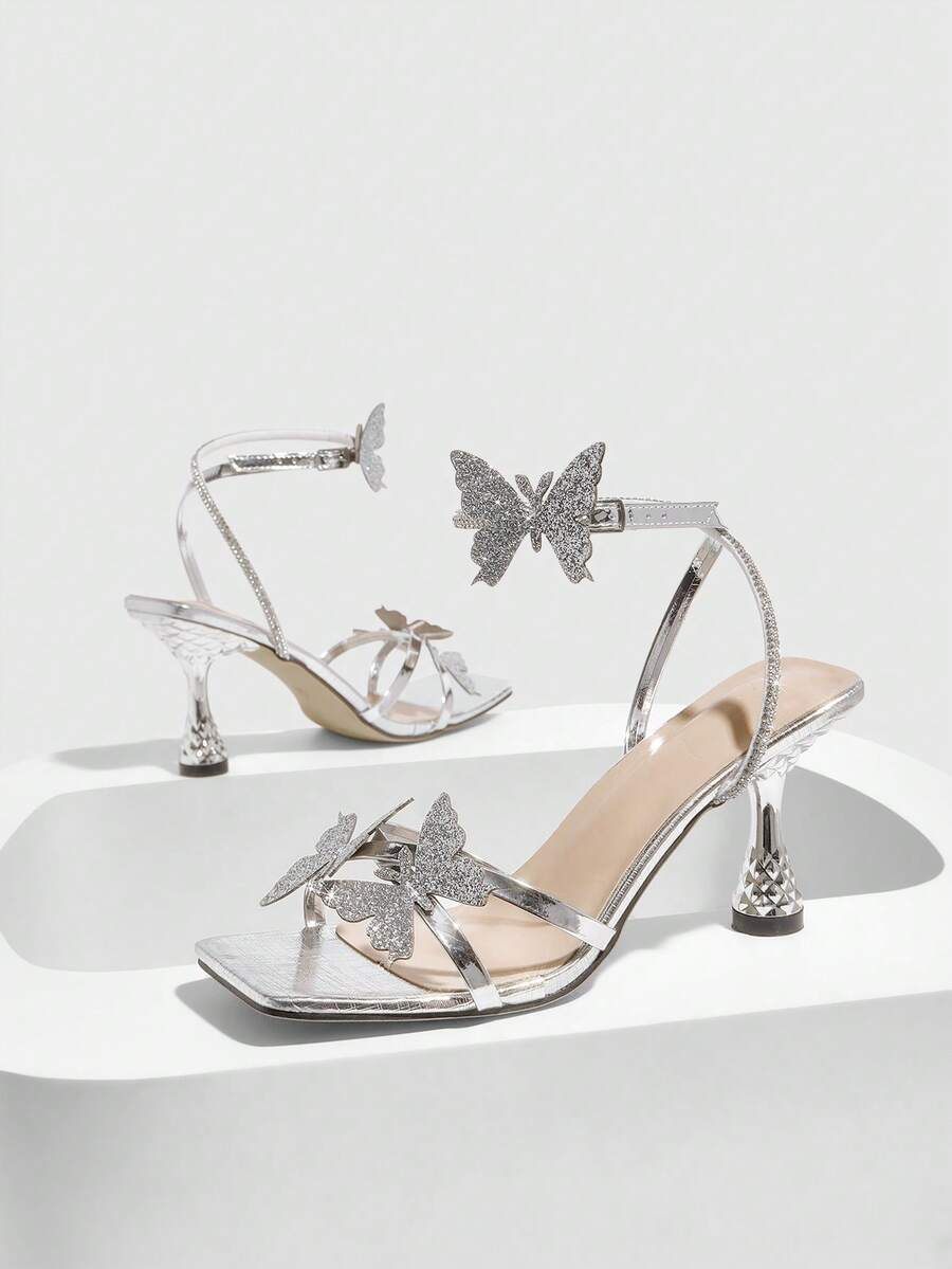 Glossy gold high heels featuring a sculptural heel, open-toe design, ankle strap buckle closure, and sparkling rhinestone butterfly embellishments.