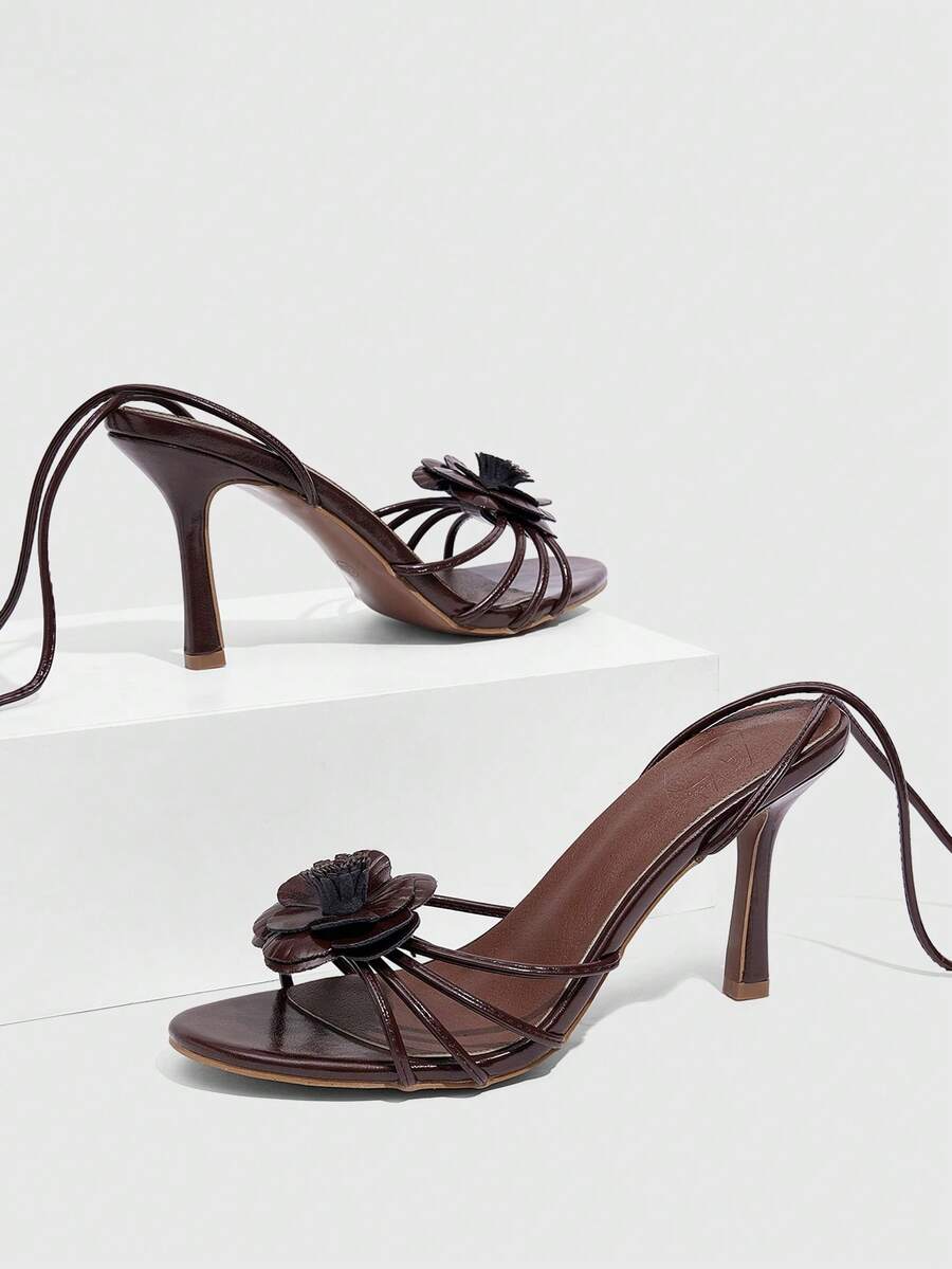 Women's round toe high heel sandals with brown flannel finish, floral trim detail, and strappy lace-up stiletto design.