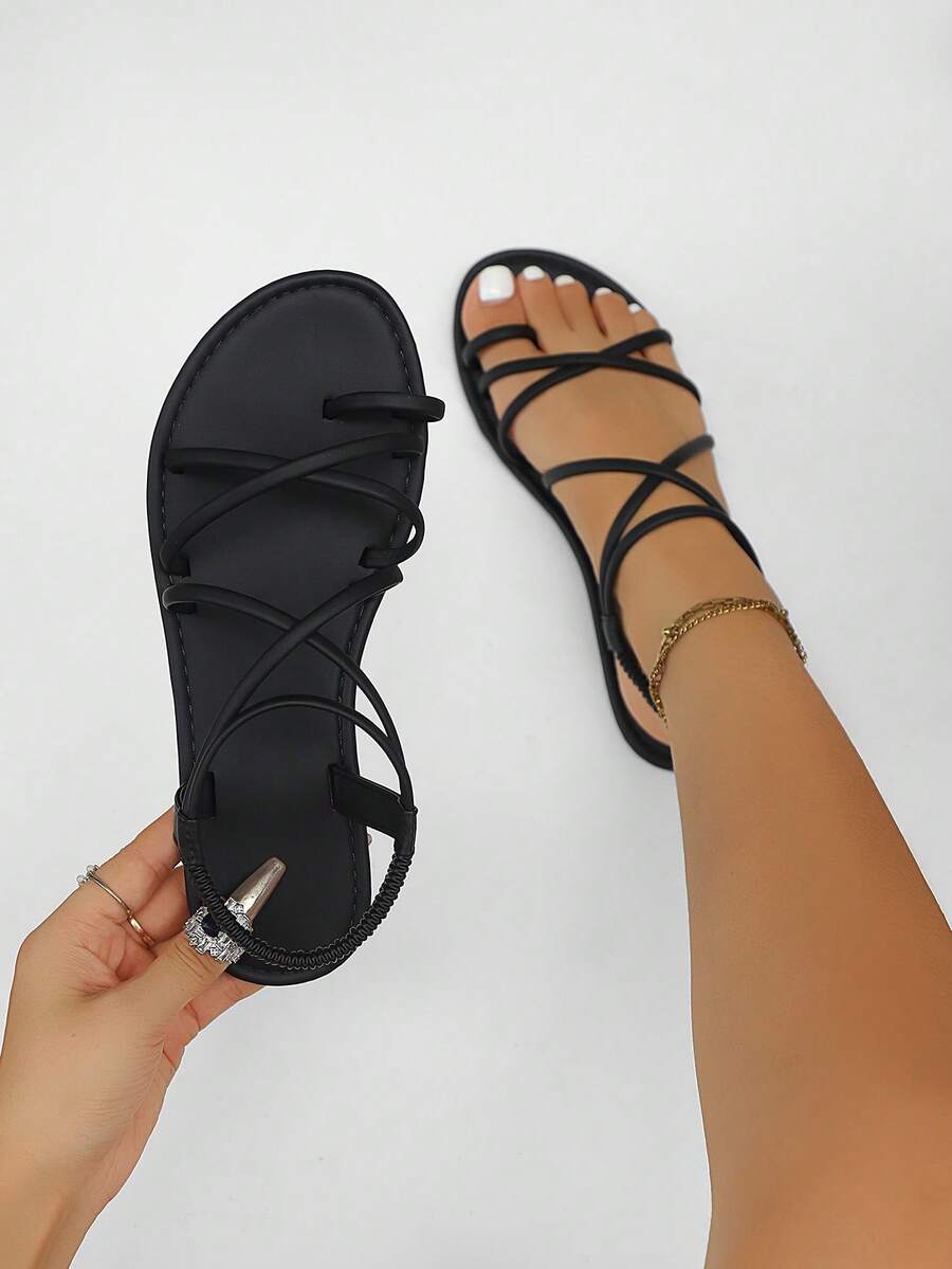 Flat sandals featuring thin criss-cross straps, elastic back strap, round toe post design, and smooth flat rubber sole.