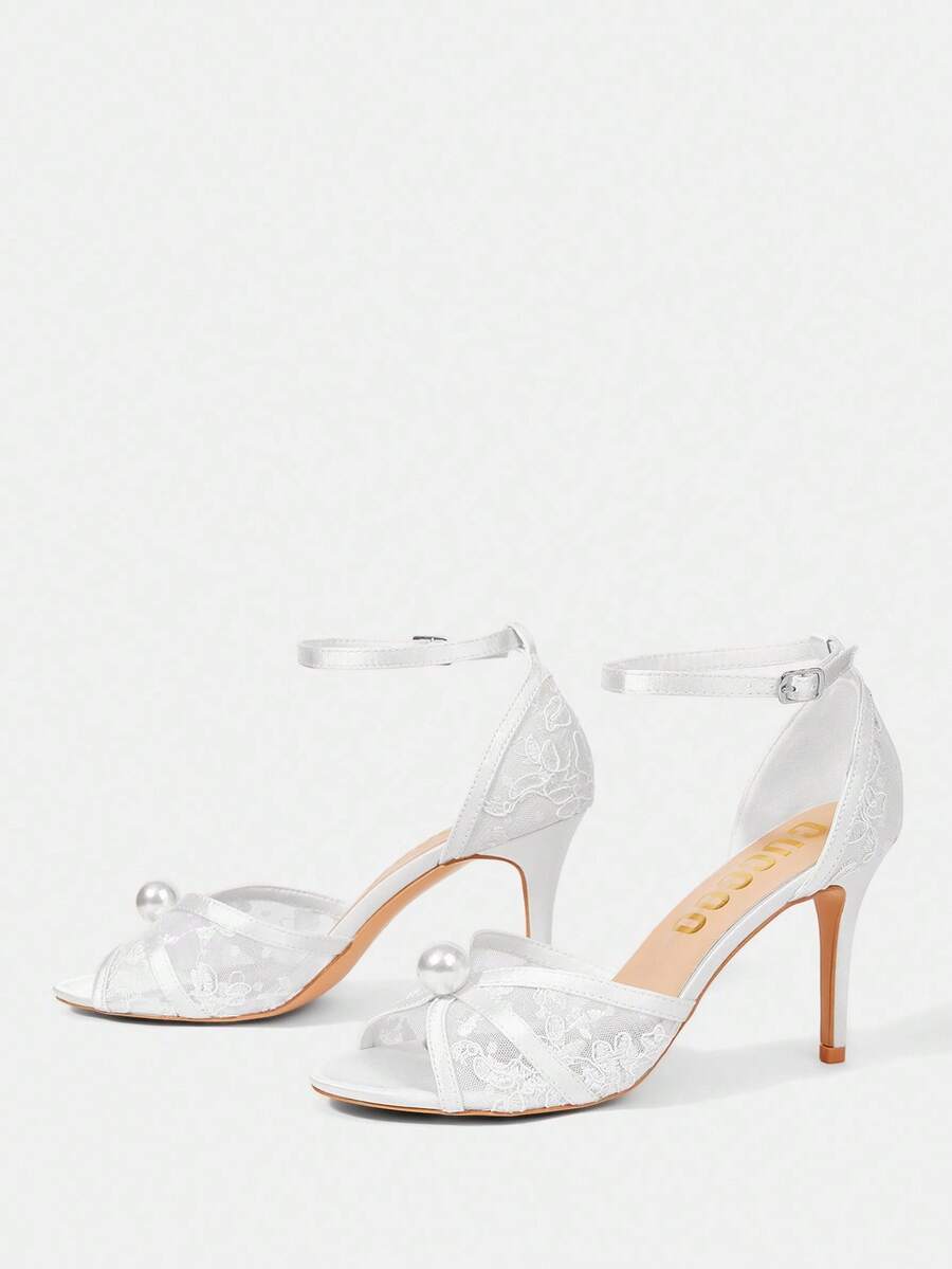 Beige high heel sandals with delicate lace overlay, pearl embellishments, stiletto heel, and adjustable ankle strap for bride and wedding party wear.