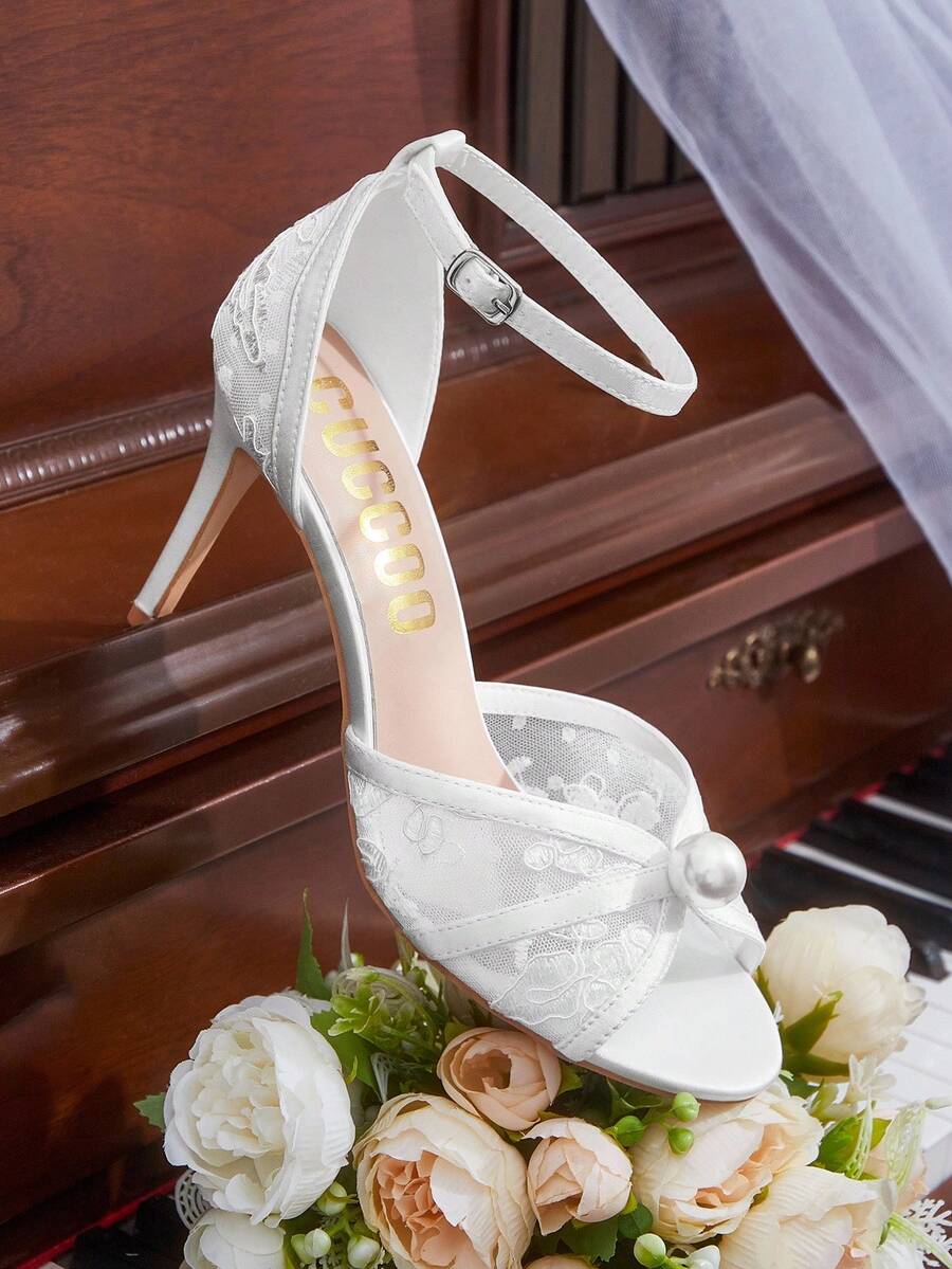 Beige high heel sandals with delicate lace overlay, pearl embellishments, stiletto heel, and adjustable ankle strap for bride and wedding party wear.