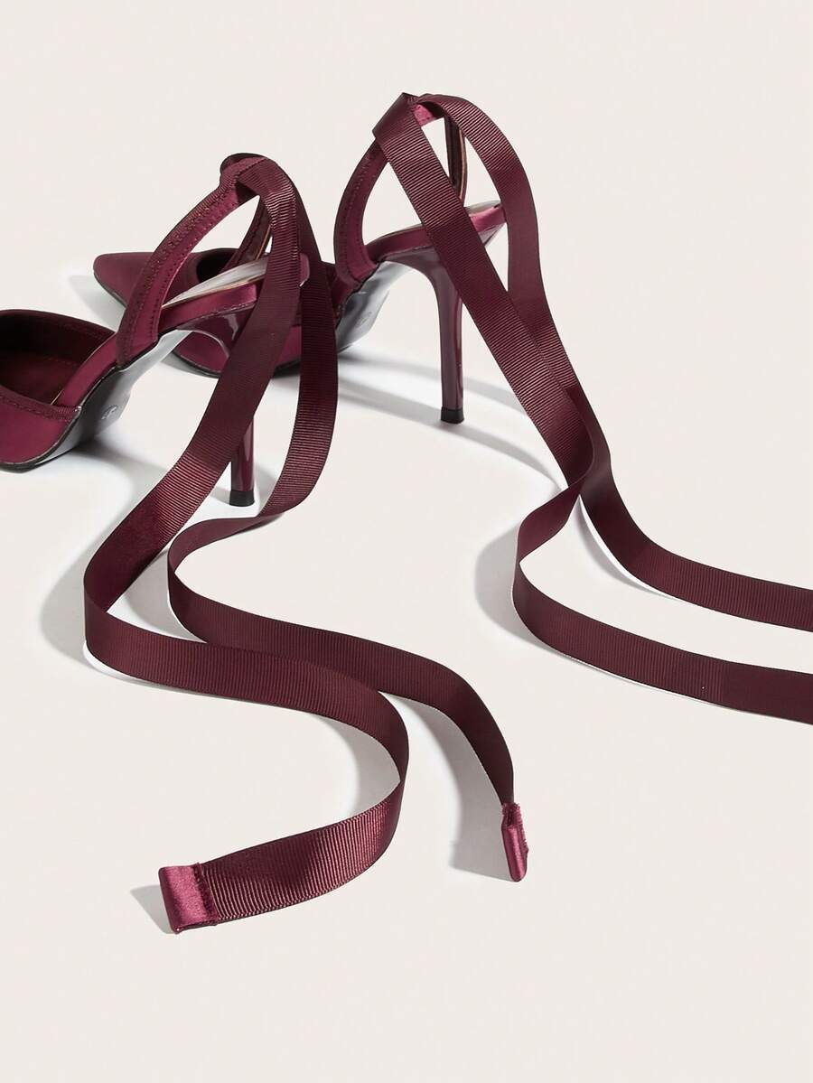 Burgundy satin pointed toe stiletto high heel pumps with a backless design and delicate bow accent.
