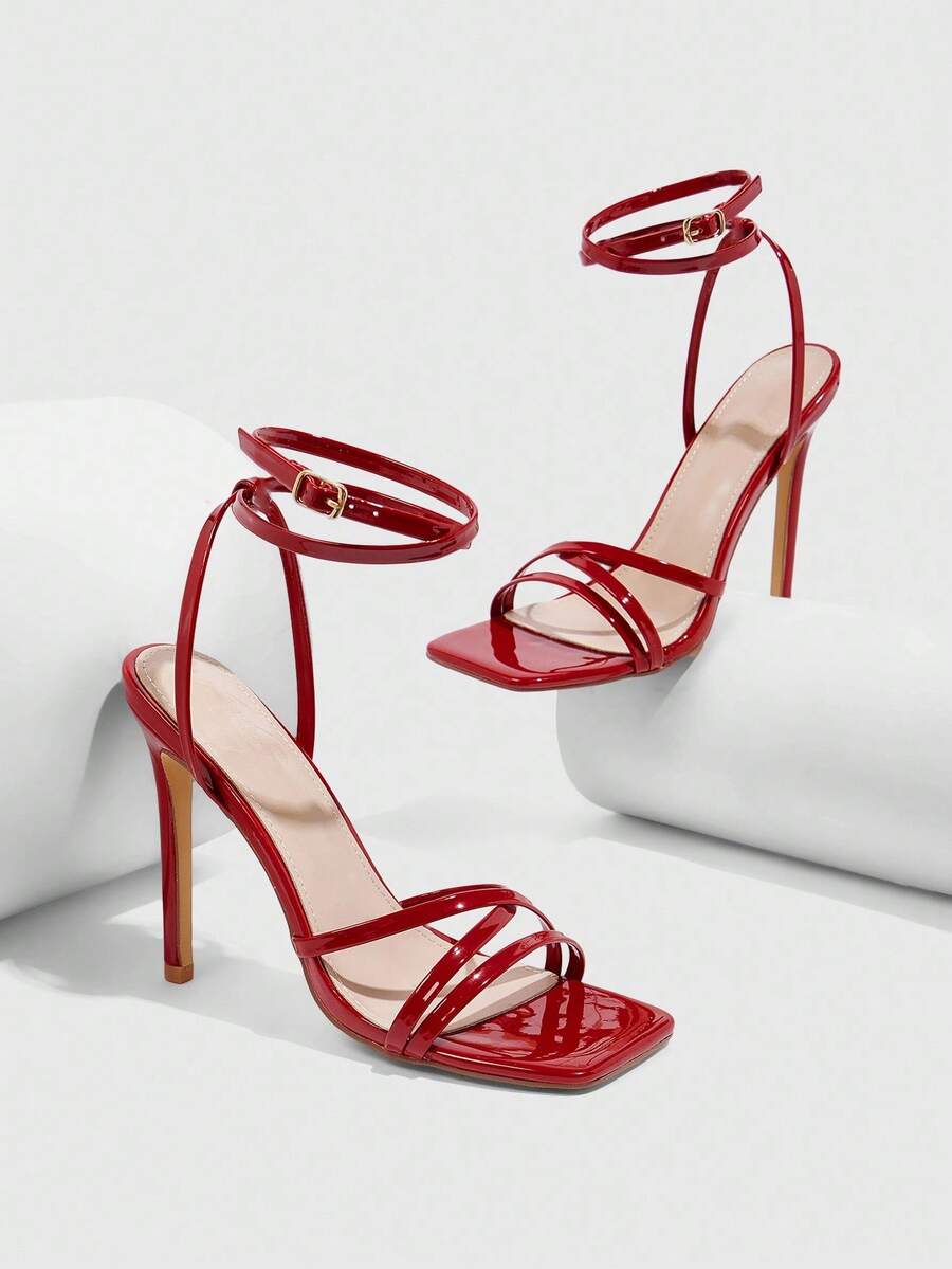 Red shiny patent leather stiletto high heel sandals featuring a square toe and criss-cross ankle strap with buckle closure.