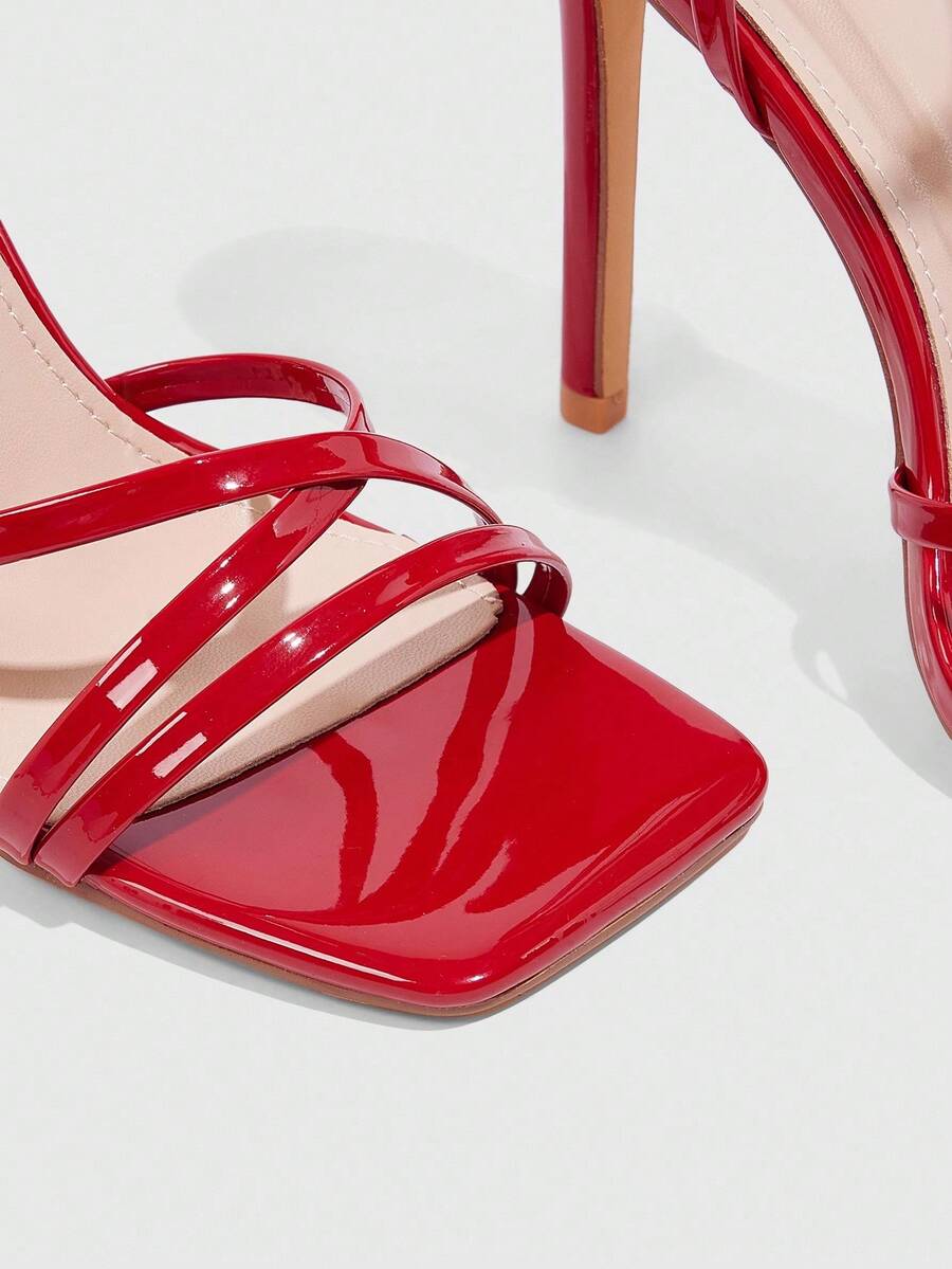 Red shiny patent leather stiletto high heel sandals featuring a square toe and criss-cross ankle strap with buckle closure.