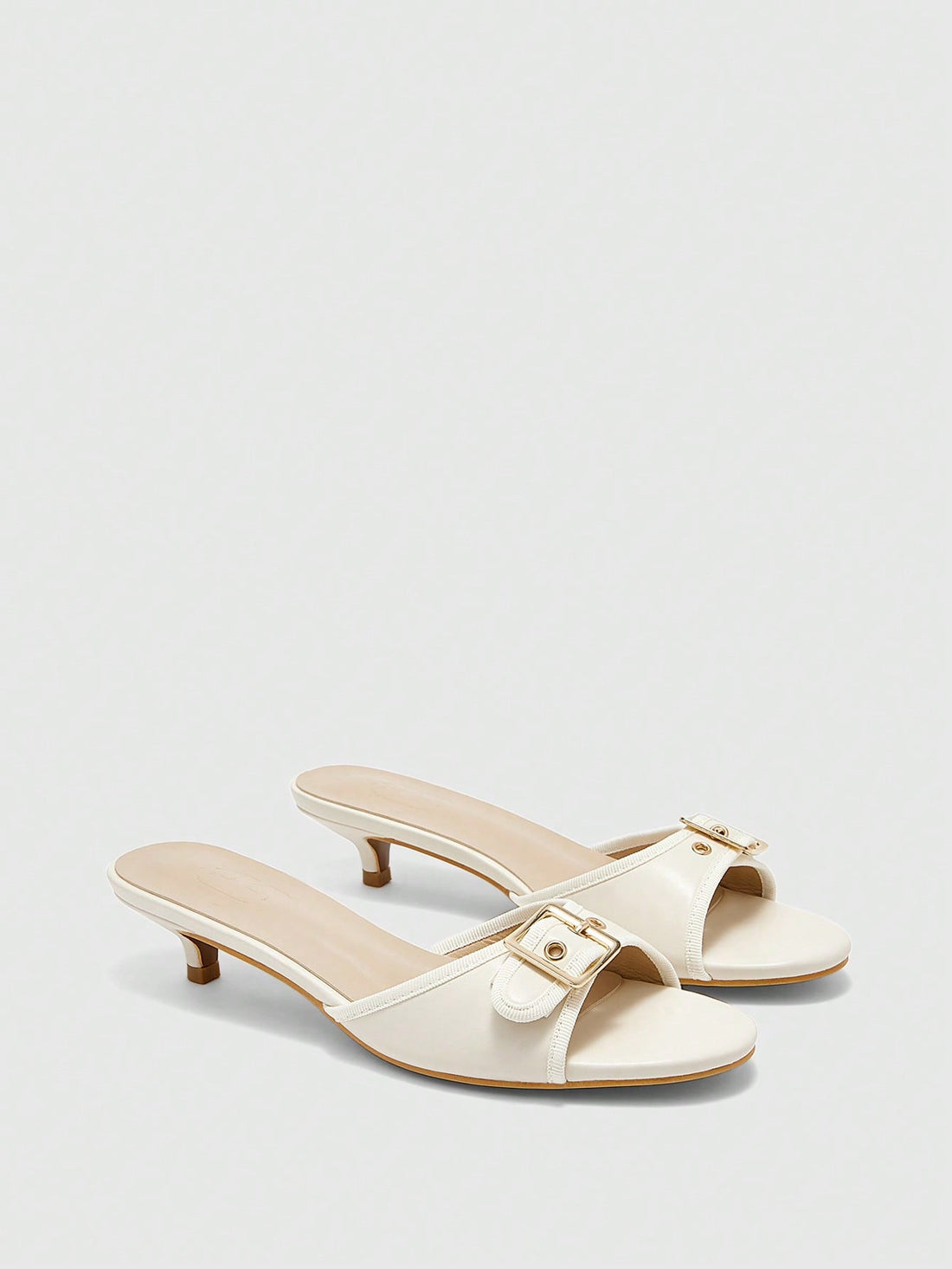 Beige women's slip-on kitten heel slide sandals featuring an accent buckle with grommet eyelets.