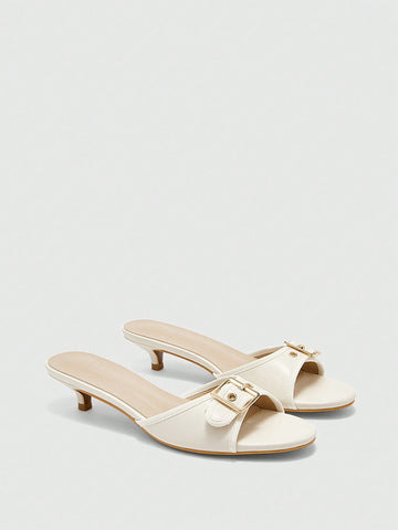 Beige women's slip-on kitten heel slide sandals featuring an accent buckle with grommet eyelets.