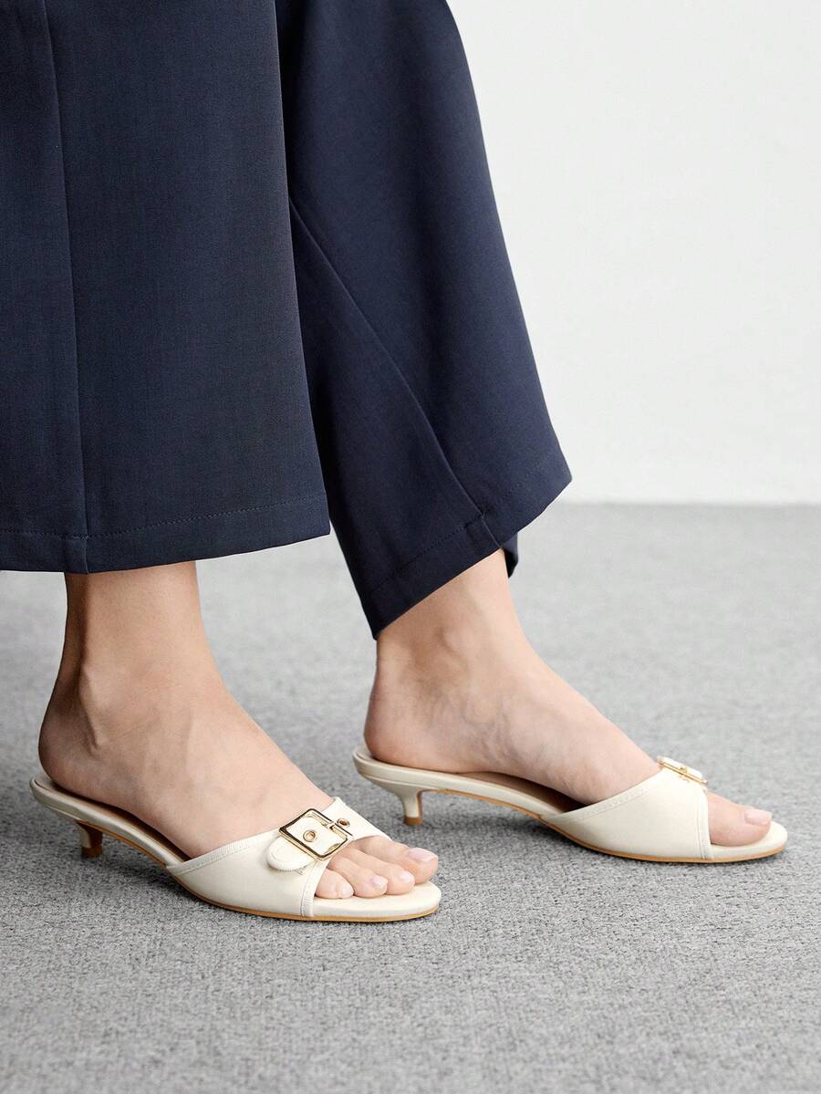 Beige women's slip-on kitten heel slide sandals featuring an accent buckle with grommet eyelets.