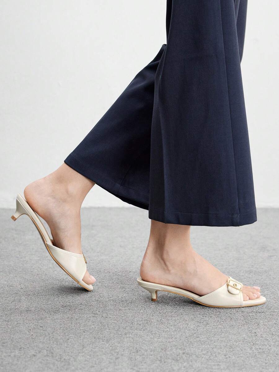 Beige women's slip-on kitten heel slide sandals featuring an accent buckle with grommet eyelets.