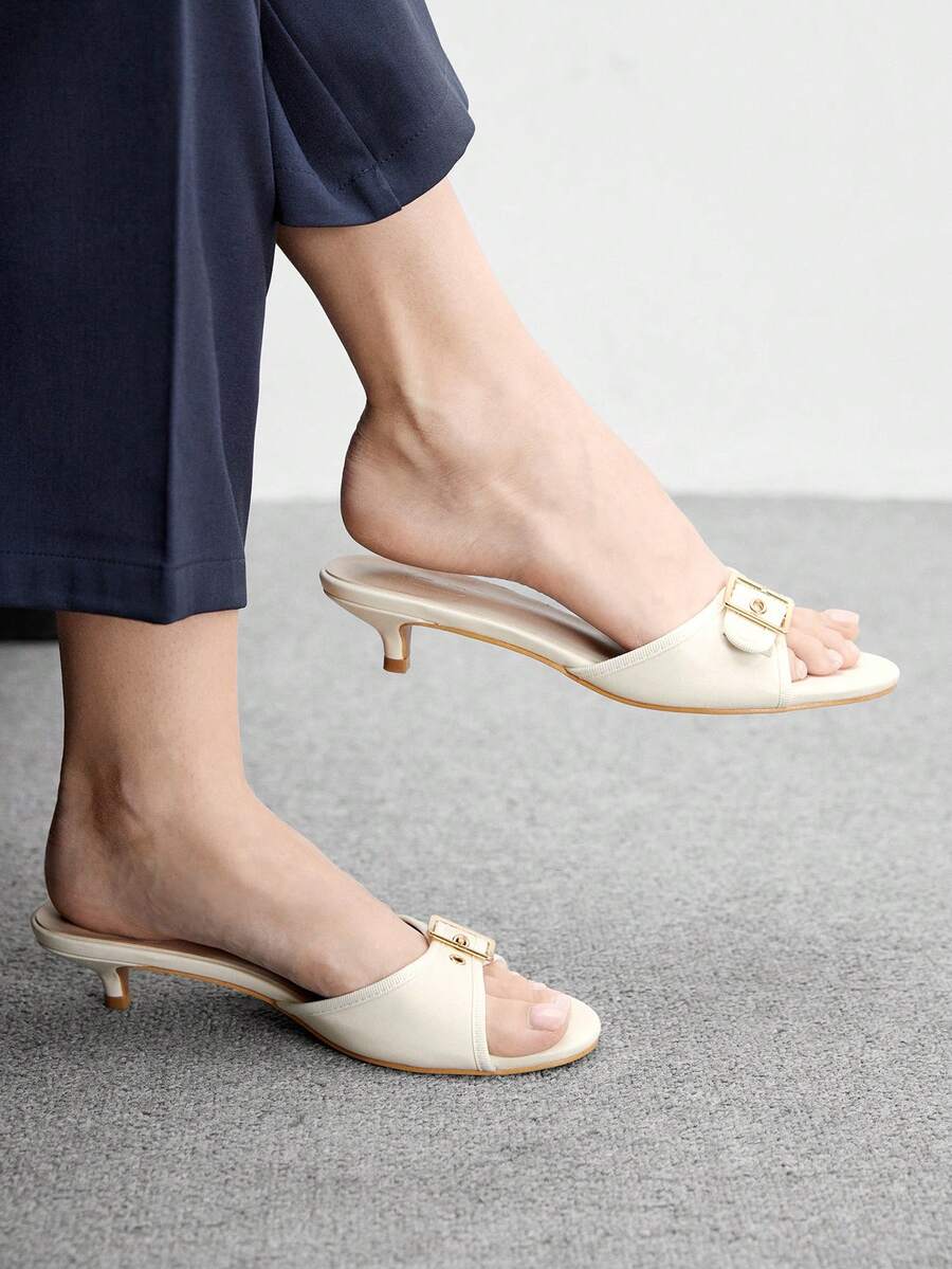 Beige women's slip-on kitten heel slide sandals featuring an accent buckle with grommet eyelets.