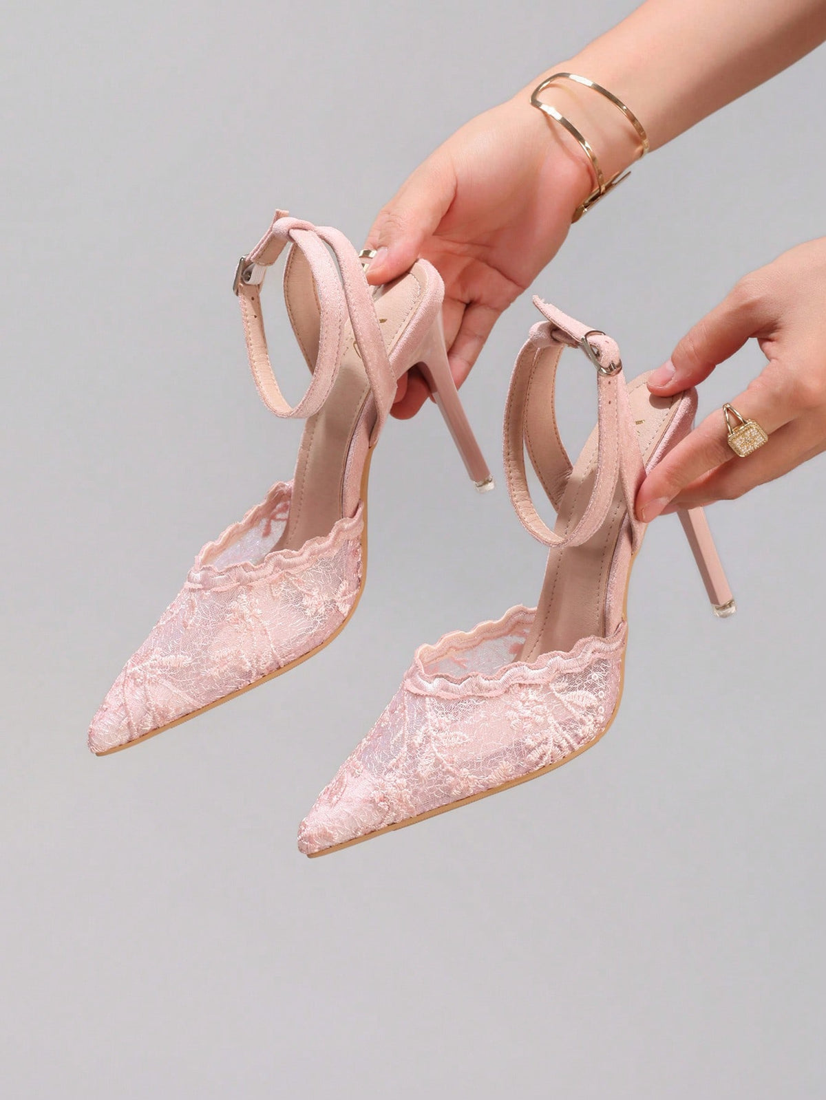 Lace embroidered high heels with thin stiletto heel, pointed toe, rhinestone embellishments, and ankle strap buckle closure.