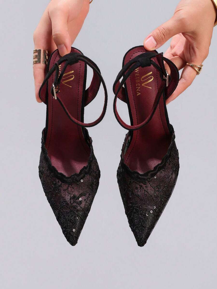 Lace embroidered high heels with thin stiletto heel, pointed toe, rhinestone embellishments, and ankle strap buckle closure.