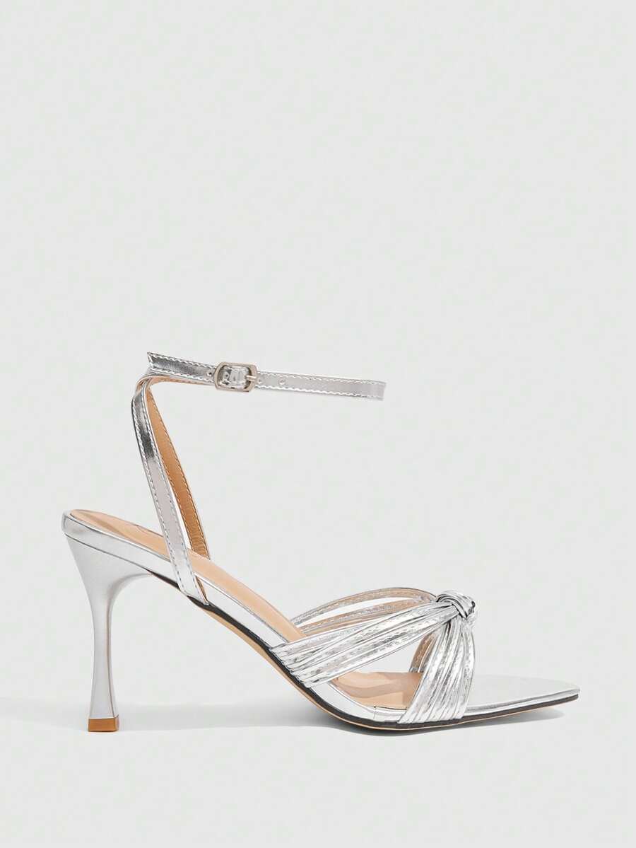 Open toe high heel sandals in champagne gold featuring a twist knot front strap, sleek stiletto heel, and adjustable ankle buckle strap.