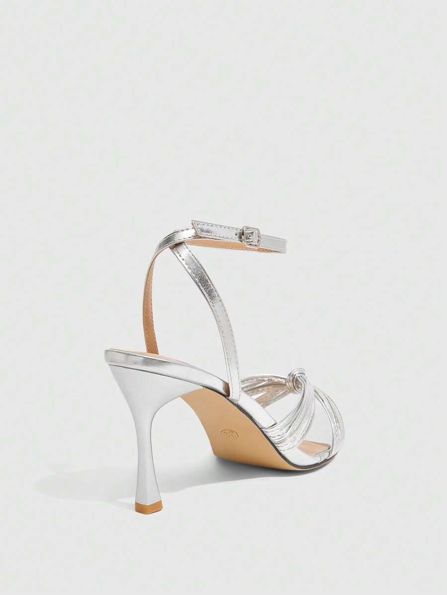 Open toe high heel sandals in champagne gold featuring a twist knot front strap, sleek stiletto heel, and adjustable ankle buckle strap.
