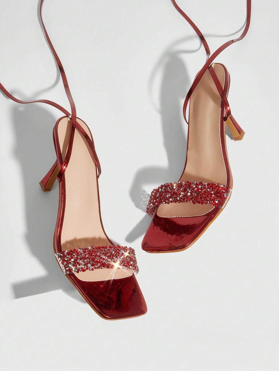 Red shiny patent leather stiletto high heel sandals featuring a square toe and criss-cross ankle strap with buckle closure.