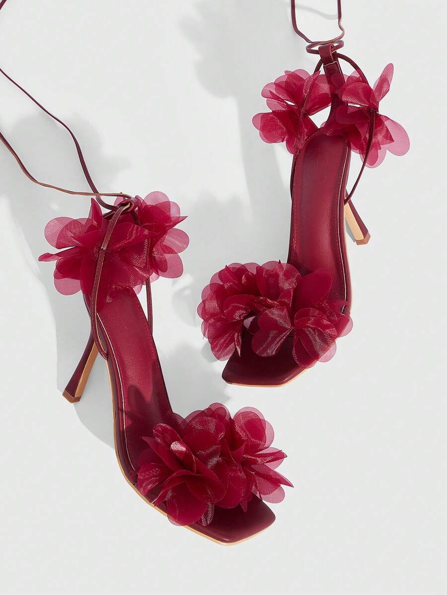 Women's open toe heeled sandals featuring 3D floral decor, satin lace-up ankle straps, and stiletto high heels.