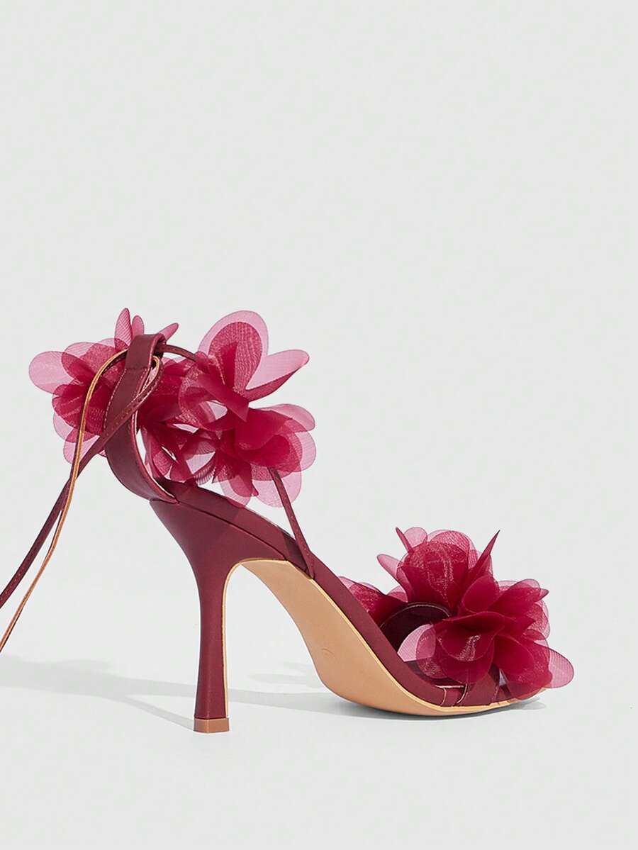 Women's open toe heeled sandals featuring 3D floral decor, satin lace-up ankle straps, and stiletto high heels.