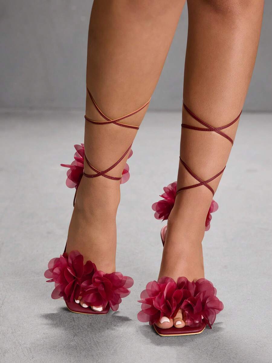 Women's open toe heeled sandals featuring 3D floral decor, satin lace-up ankle straps, and stiletto high heels.