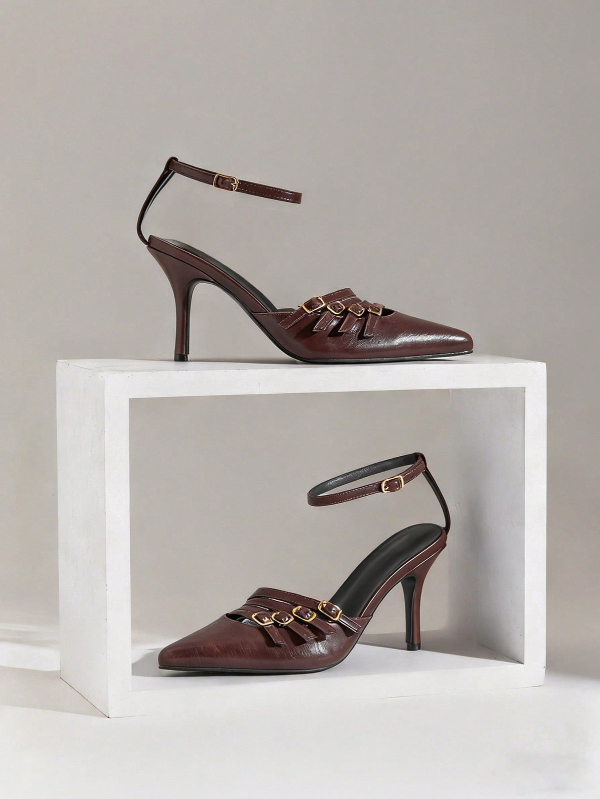 Women's pointed toe stiletto heel slingback pumps in chocolate brown with double metal buckle strap details.