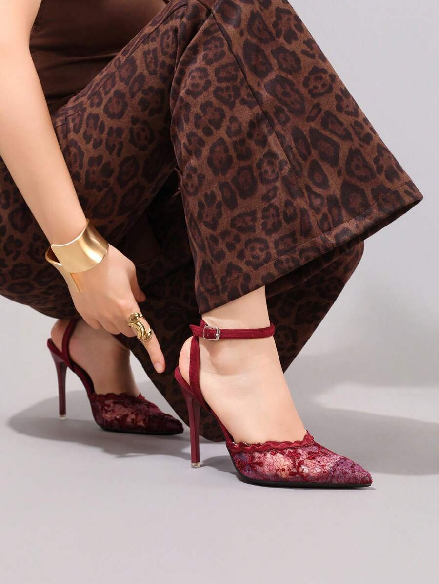 Lace embroidered high heels with thin stiletto heel, pointed toe, rhinestone embellishments, and ankle strap buckle closure.