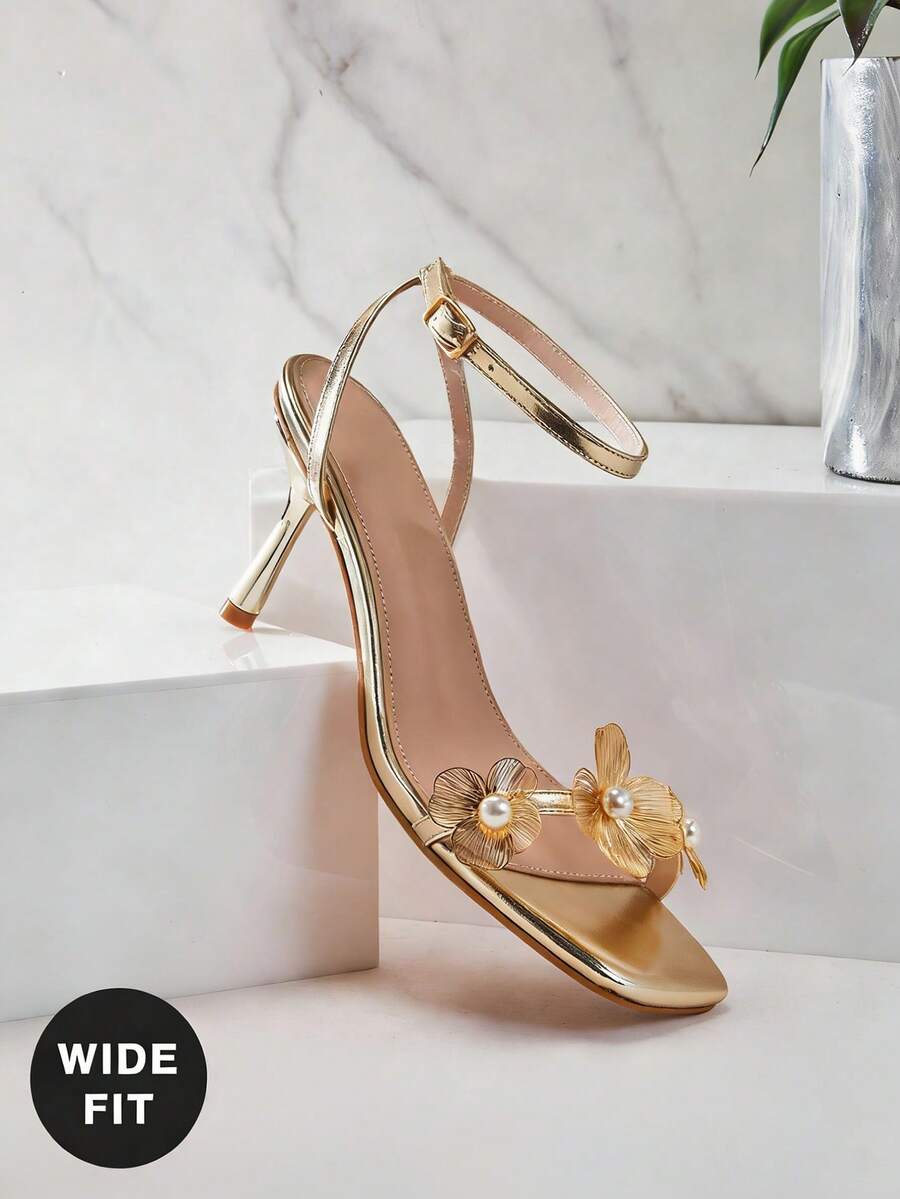 Women's metallic gold wide-fit high heeled sandals featuring stiletto heels, open toe straps, and elegant floral appliques.