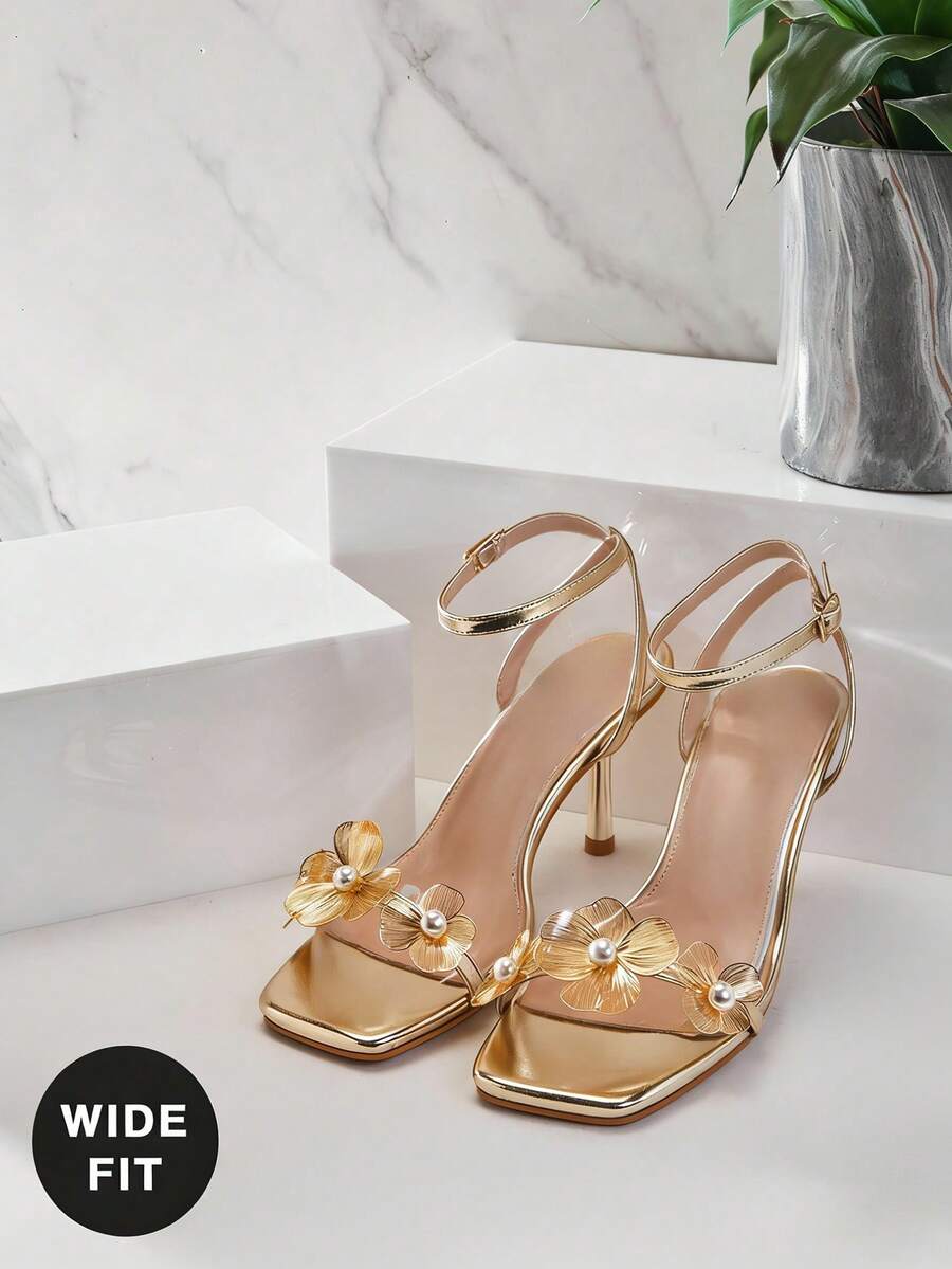 Women's metallic gold wide-fit high heeled sandals featuring stiletto heels, open toe straps, and elegant floral appliques.