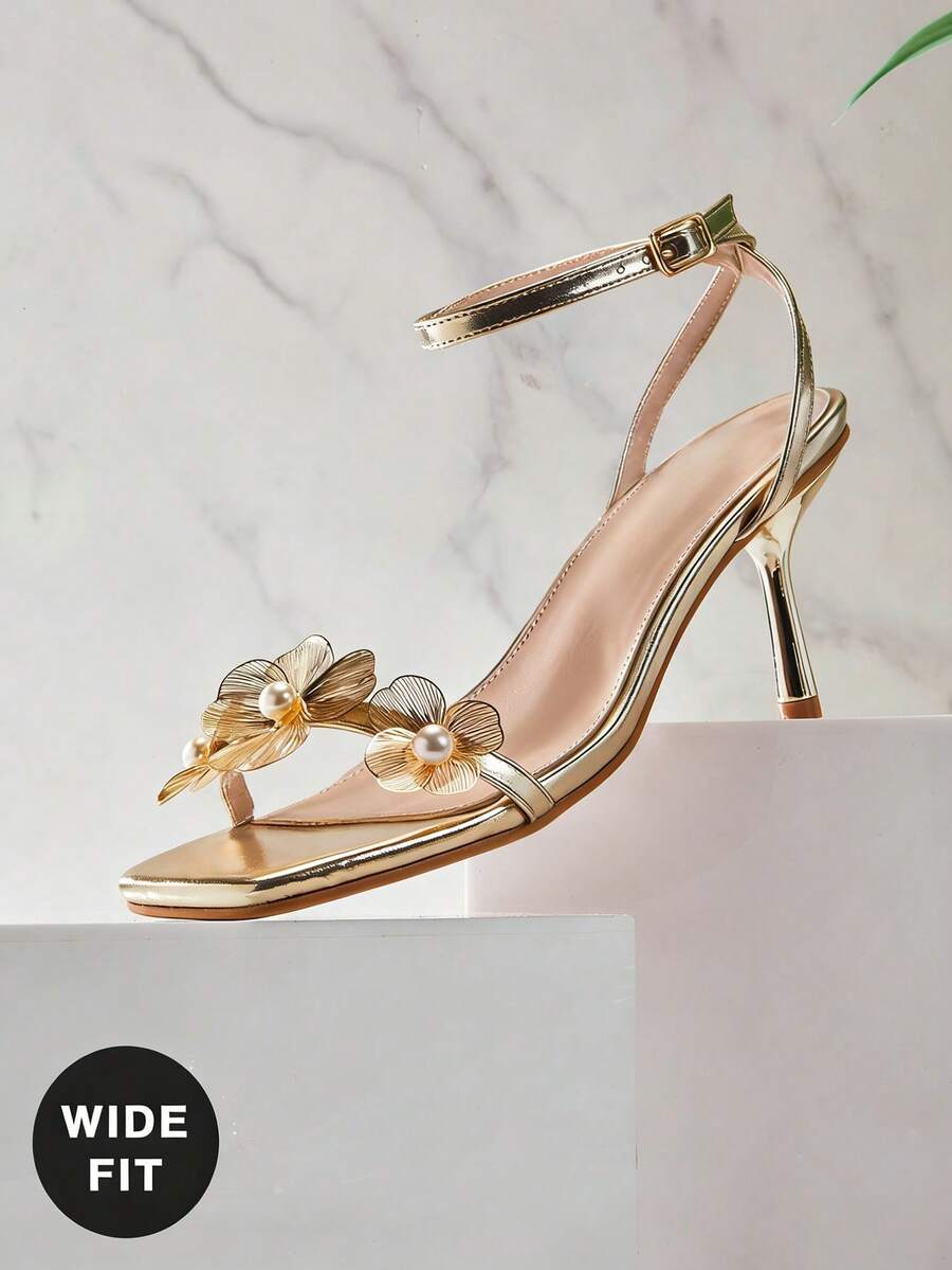 Women's metallic gold wide-fit high heeled sandals featuring stiletto heels, open toe straps, and elegant floral appliques.