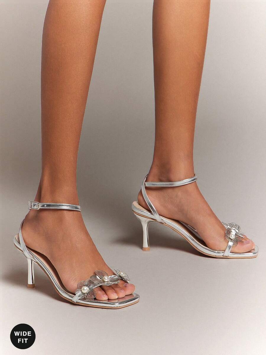 Women's metallic gold wide-fit high heeled sandals featuring stiletto heels, open toe straps, and elegant floral appliques.