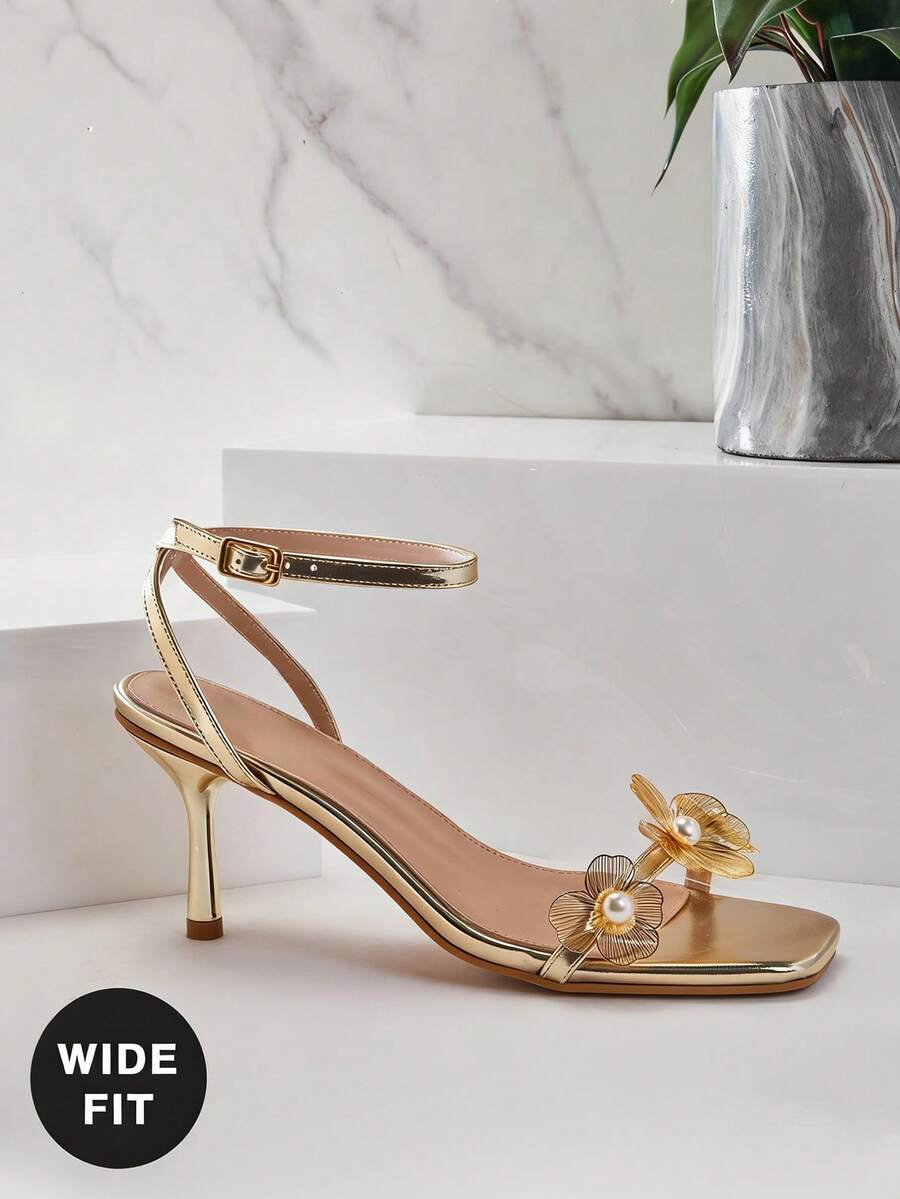 Women's metallic gold wide-fit high heeled sandals featuring stiletto heels, open toe straps, and elegant floral appliques.