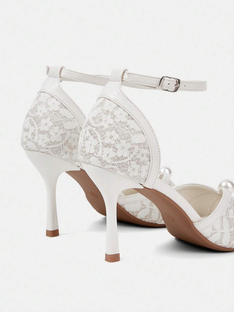Beige high heel sandals with delicate lace overlay, pearl embellishments, stiletto heel, and adjustable ankle strap for bride and wedding party wear.