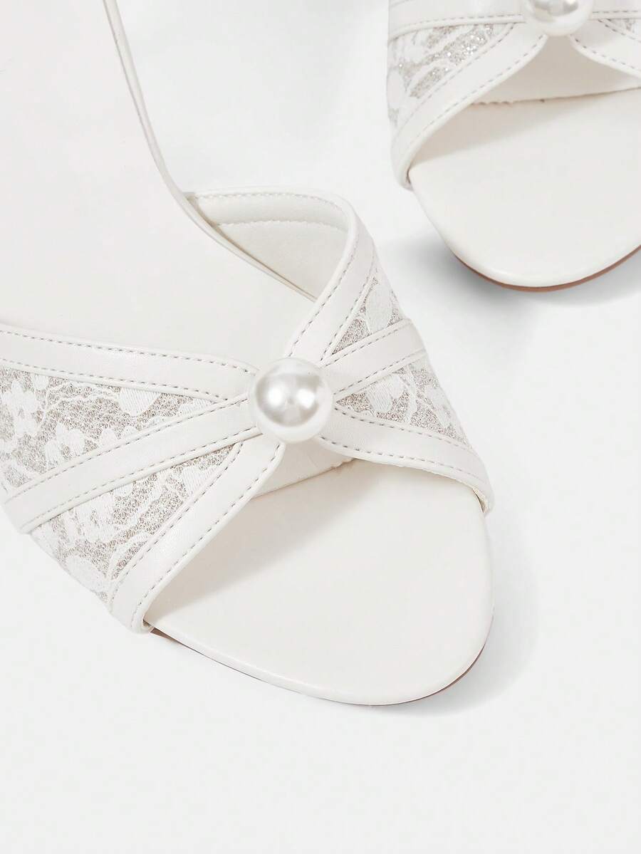 Beige high heel sandals with delicate lace overlay, pearl embellishments, stiletto heel, and adjustable ankle strap for bride and wedding party wear.