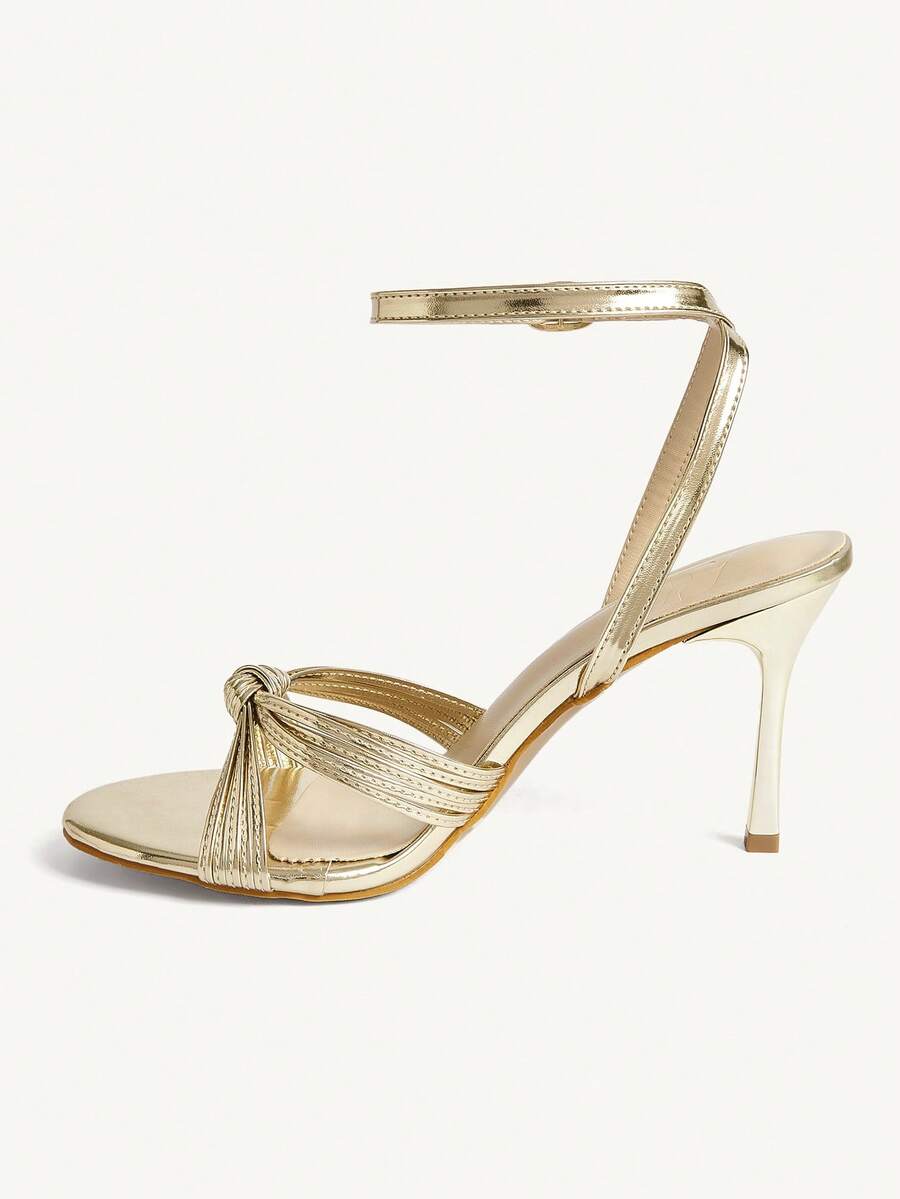 Women's champagne stiletto high heel sandals featuring knotted cross-over straps, open round toe, and adjustable ankle buckle strap.