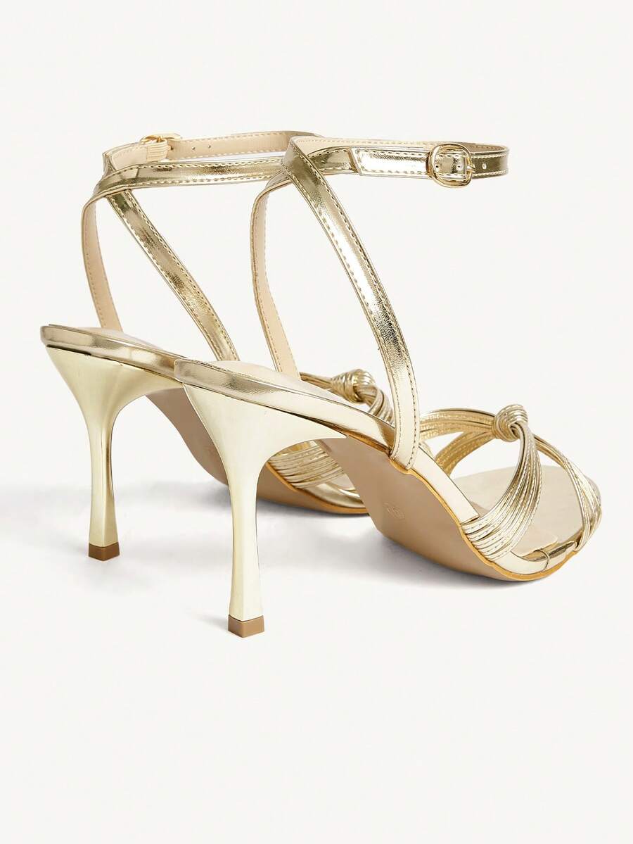 Women's champagne stiletto high heel sandals featuring knotted cross-over straps, open round toe, and adjustable ankle buckle strap.
