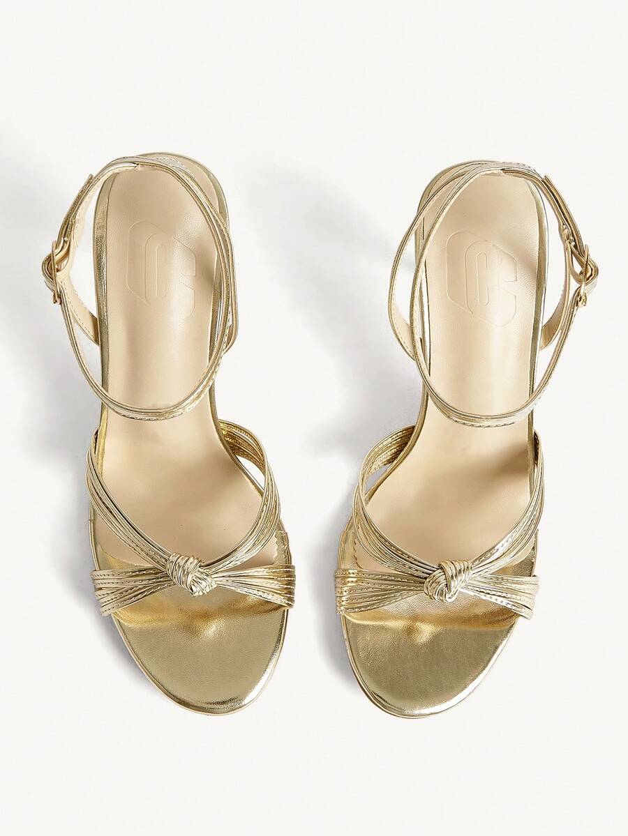 Women's champagne stiletto high heel sandals featuring knotted cross-over straps, open round toe, and adjustable ankle buckle strap.
