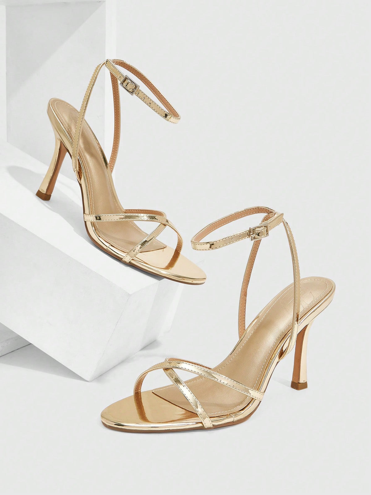 Pair of cream open-toe heeled sandals featuring crisscross front straps, a sleek stiletto high heel, and an adjustable ankle strap with buckle closure.