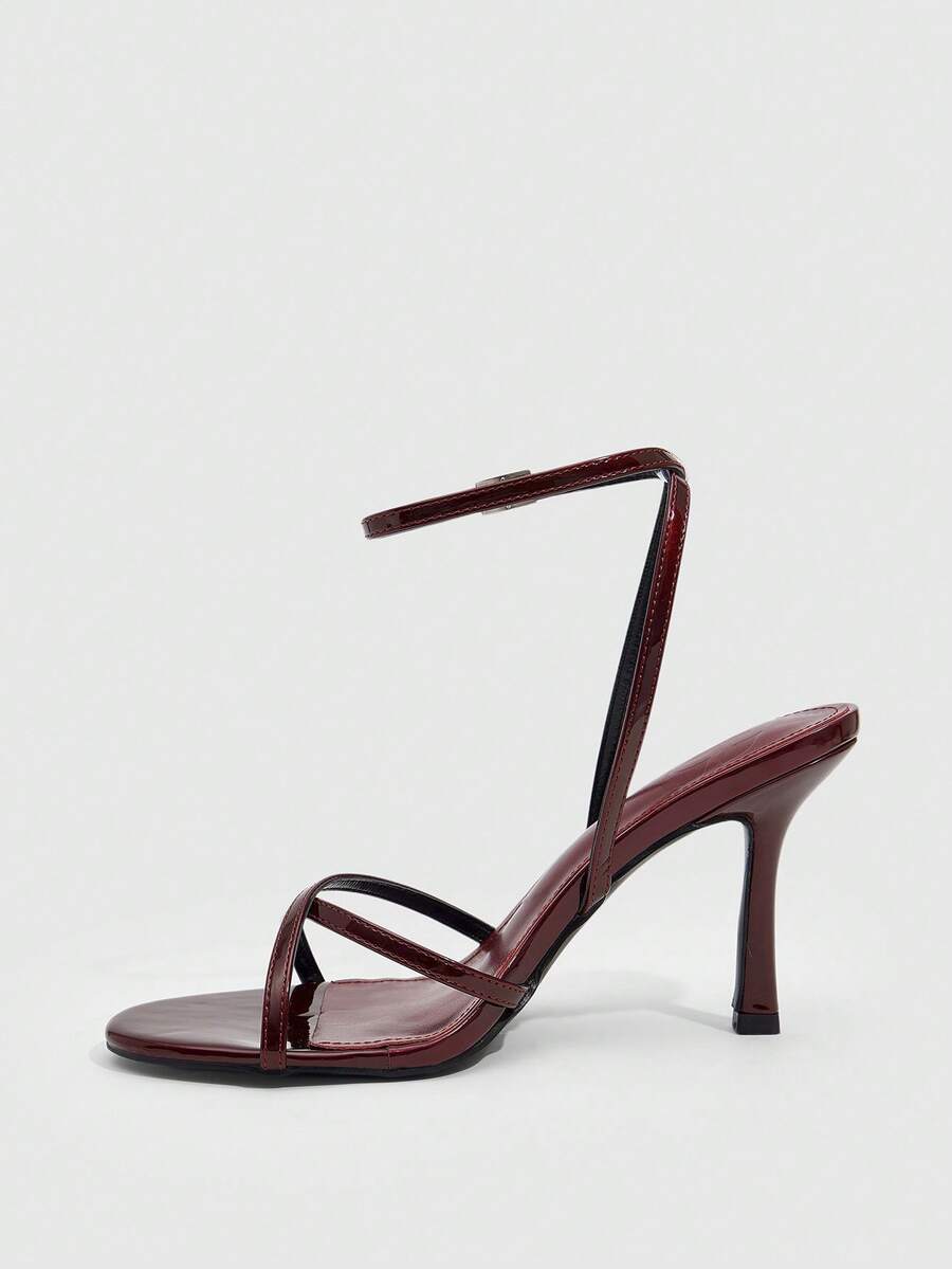 Pair of cream open-toe heeled sandals featuring crisscross front straps, a sleek stiletto high heel, and an adjustable ankle strap with buckle closure.
