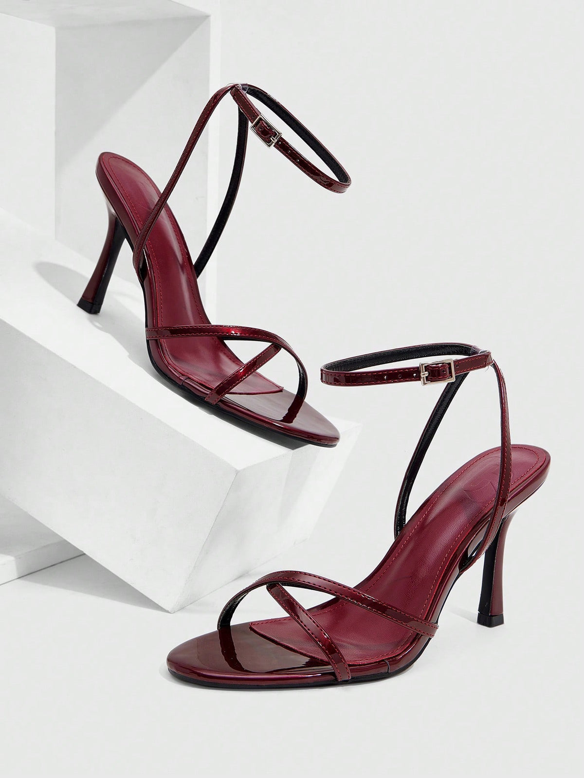 Pair of cream open-toe heeled sandals featuring crisscross front straps, a sleek stiletto high heel, and an adjustable ankle strap with buckle closure.