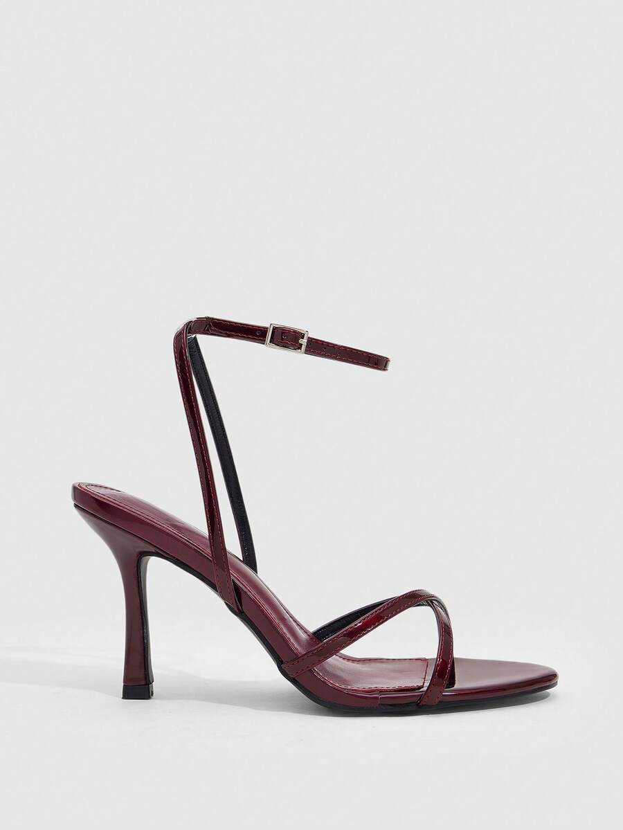 Pair of cream open-toe heeled sandals featuring crisscross front straps, a sleek stiletto high heel, and an adjustable ankle strap with buckle closure.