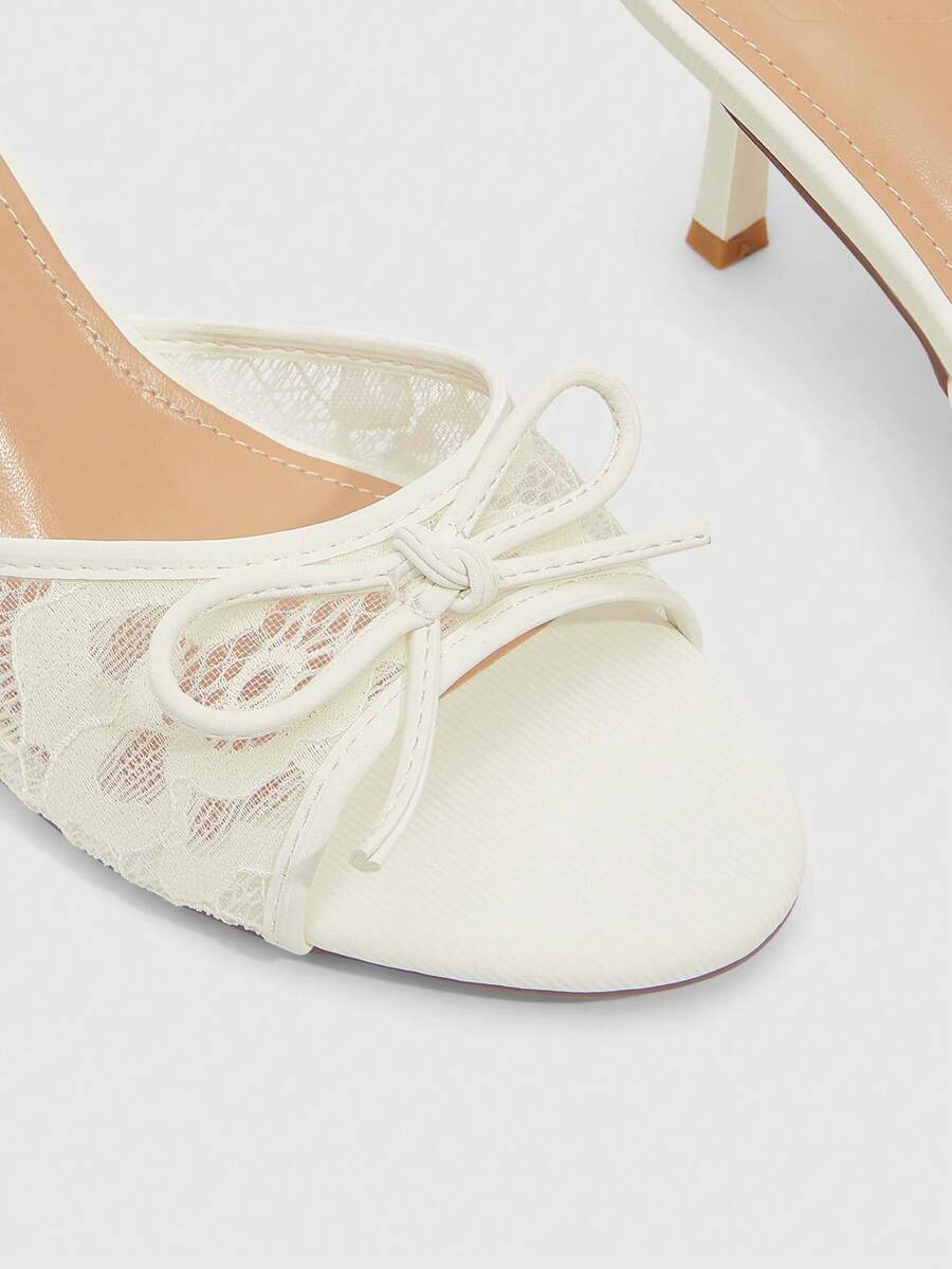 Open toe high heel slide sandals featuring lace details and a bow accent on the upper strap.