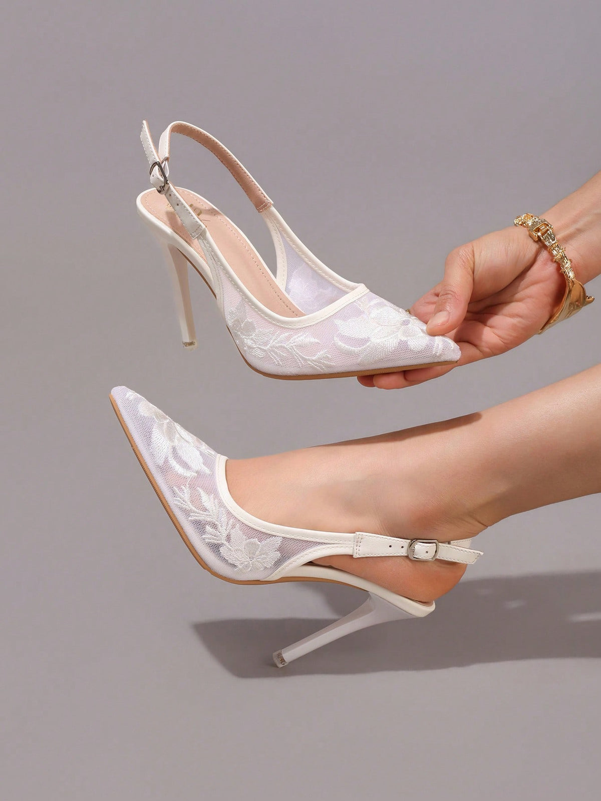 Lace embroidered high heels with thin stiletto heel, pointed toe, rhinestone embellishments, and ankle strap buckle closure.