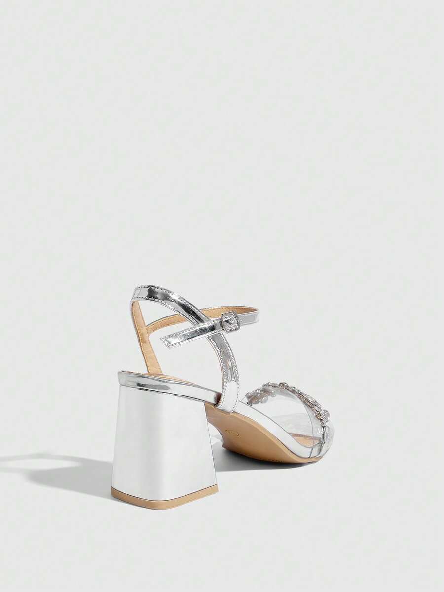 Pair of women's silver open-toe high-heeled sandals featuring sparkling rhinestone details, lace-up ankle straps, and a sturdy thick chunky heel.