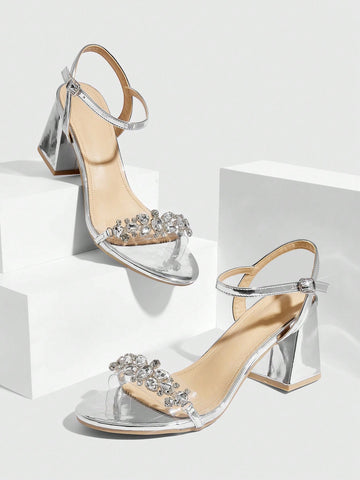 Pair of women's silver open-toe high-heeled sandals featuring sparkling rhinestone details, lace-up ankle straps, and a sturdy thick chunky heel.
