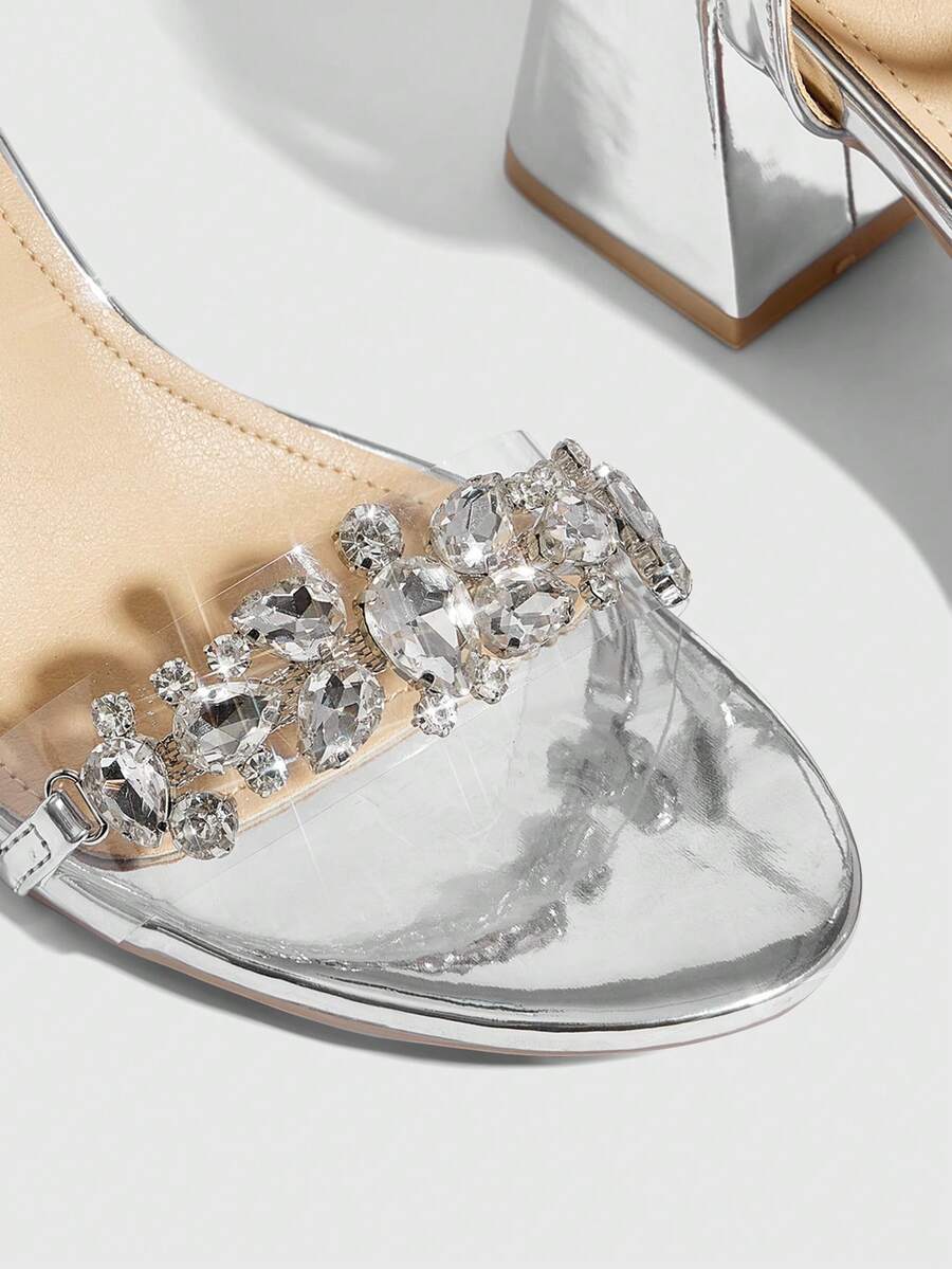 Pair of women's silver open-toe high-heeled sandals featuring sparkling rhinestone details, lace-up ankle straps, and a sturdy thick chunky heel.