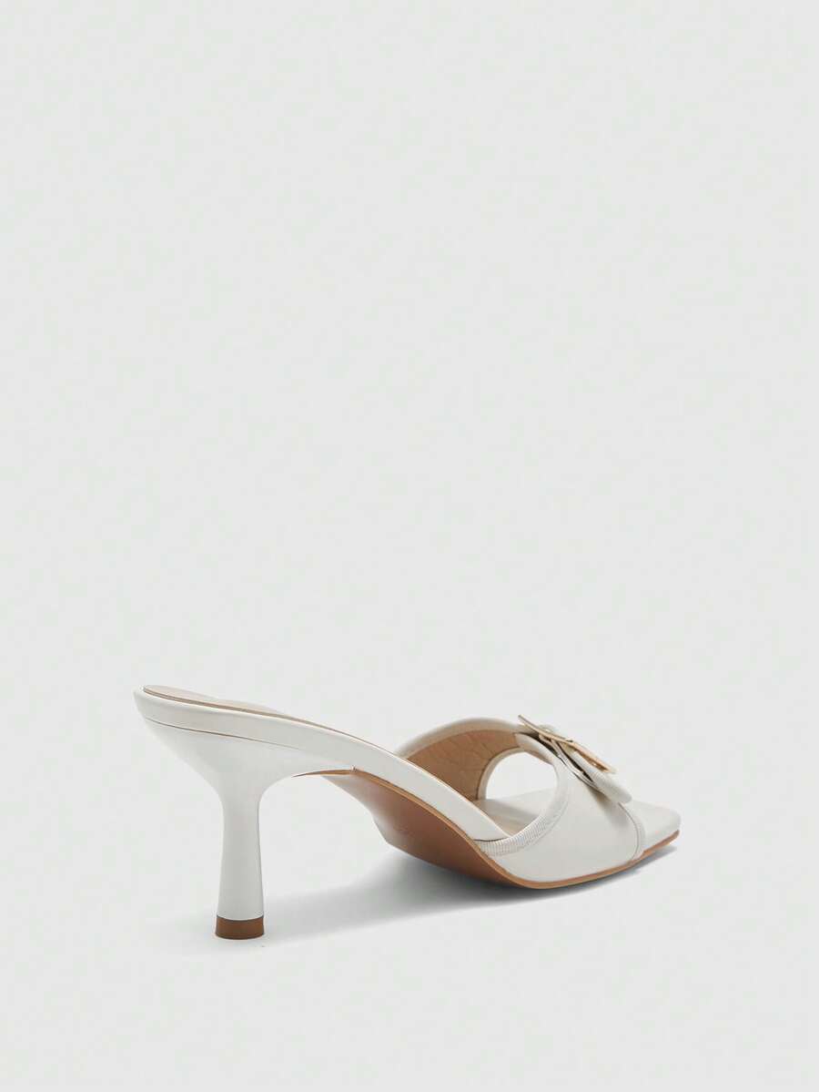Beige women's slip-on kitten heel slide sandals featuring an accent buckle with grommet eyelets.