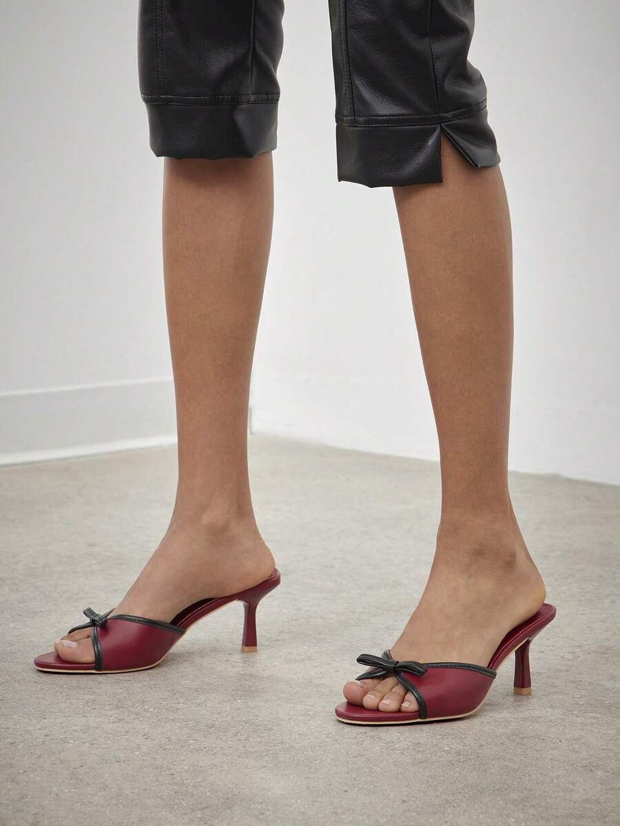 Black pointy toe kitten heel shoes for women featuring a sleek cut out mule design and glossy patent leather finish.