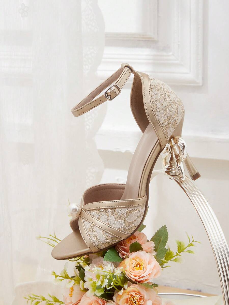 Beige high heel sandals with delicate lace overlay, pearl embellishments, stiletto heel, and adjustable ankle strap for bride and wedding party wear.