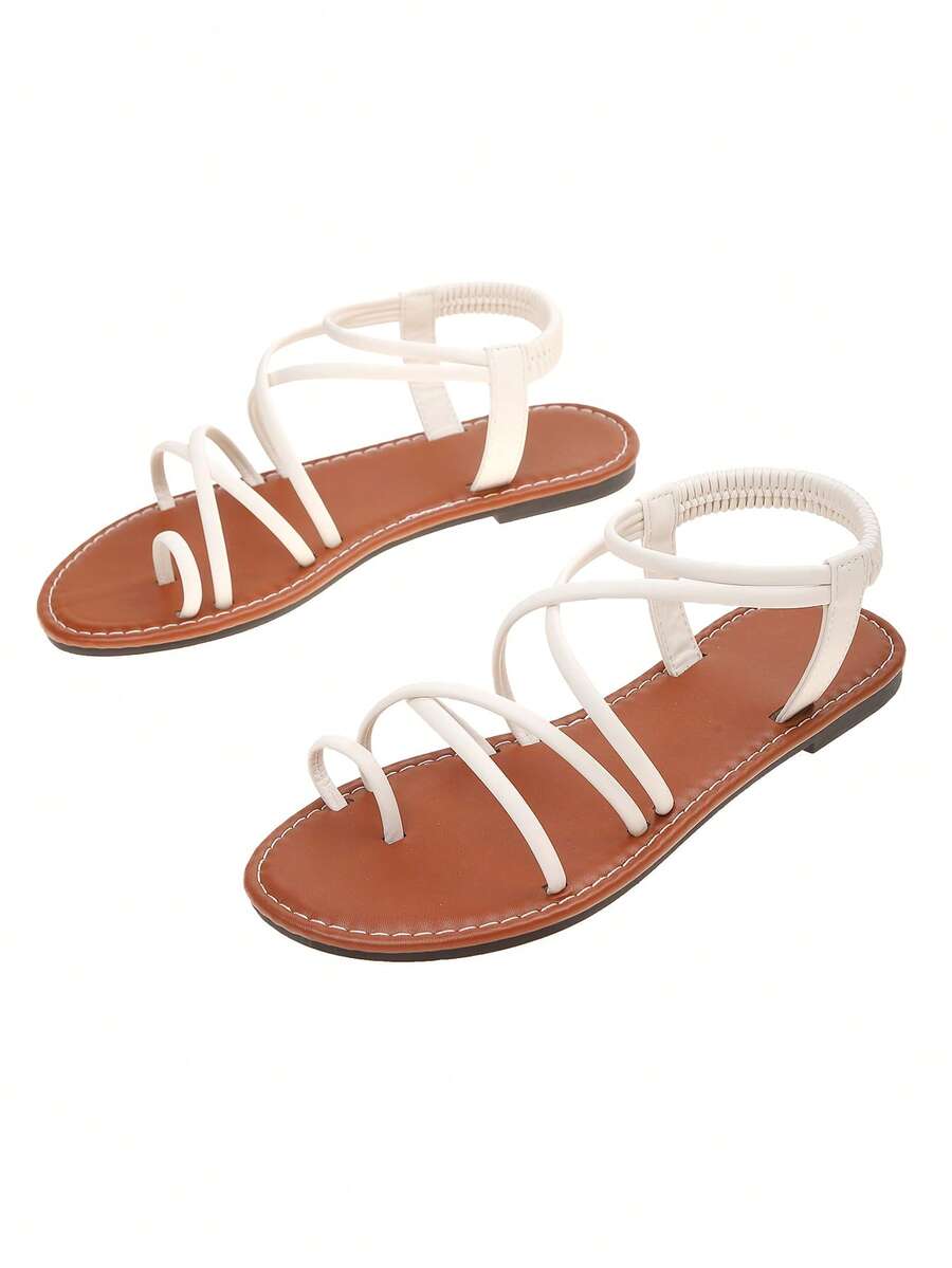 Flat sandals featuring thin criss-cross straps, elastic back strap, round toe post design, and smooth flat rubber sole.