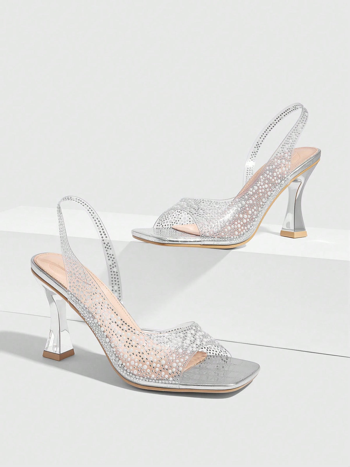 Women's square toe heeled sandals with clear straps, sparkling rhinestone embellishments, and a high pyramid heel.